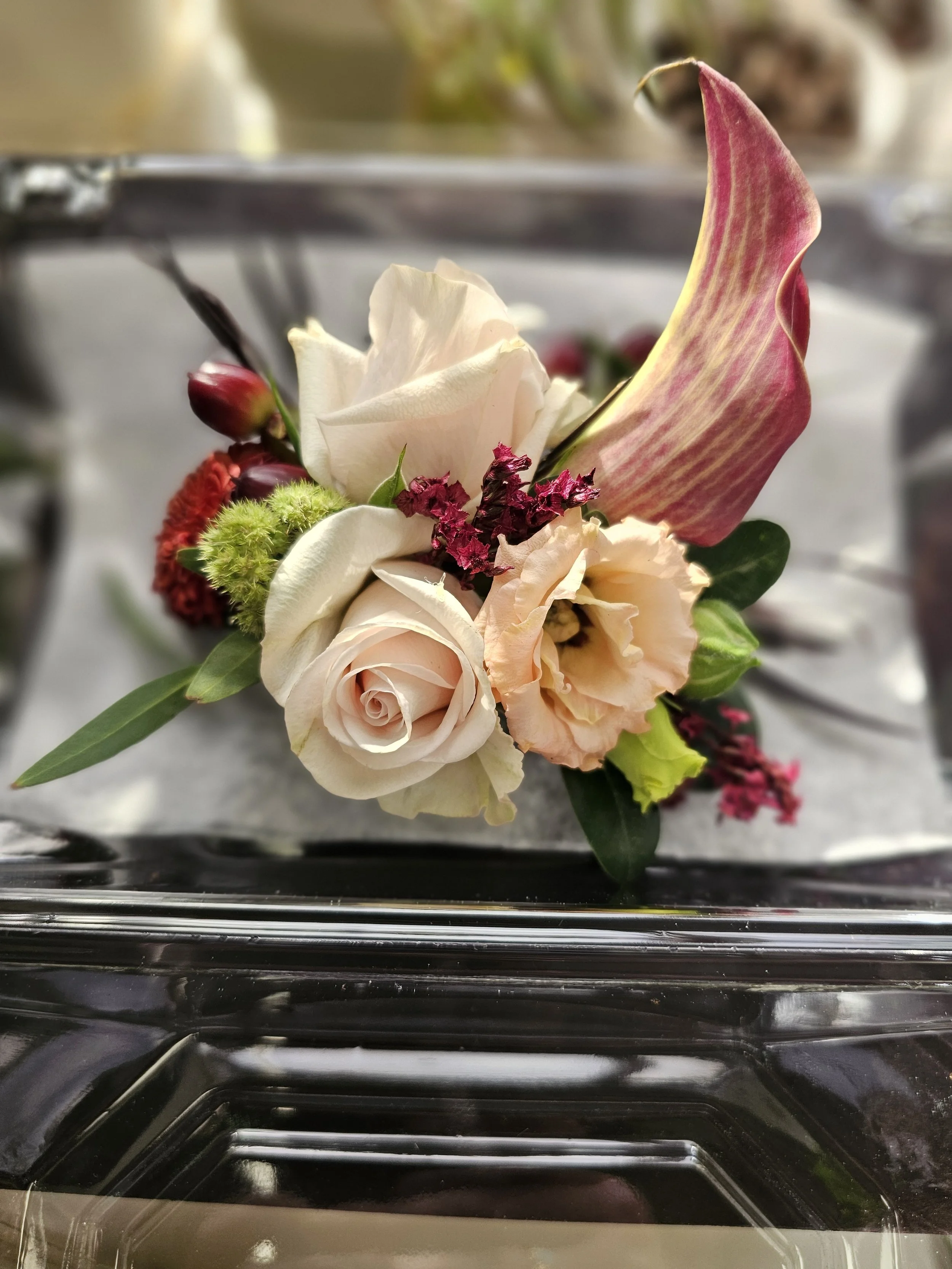 A floral arrangement with white, pink, and red flowers, including a white rose, a pink calla lily, and other assorted flowers and greenery, placed on a reflective surface.