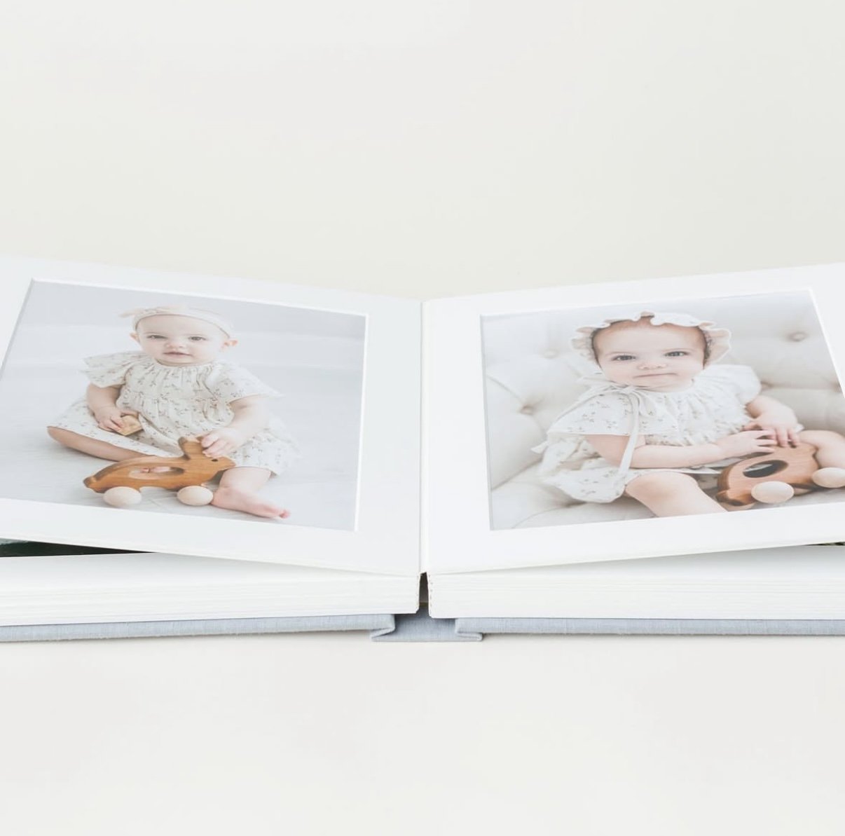 Open photo album with images of a baby in a white outfit holding a wooden toy.