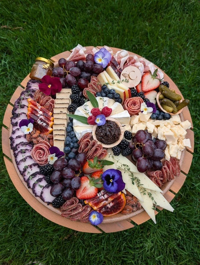 A cheese and fruit platter with grapes, strawberries, blackberries, and edible flowers on a wooden board.