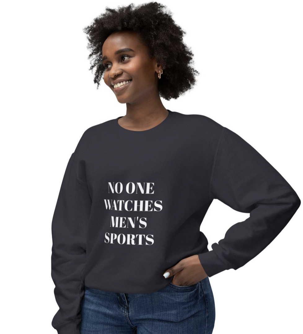 A woman wearing a black sweatshirt with the phrase 'No One Watches Men's Sports' printed in white letters, smiling and standing with one hand in her jean pocket.