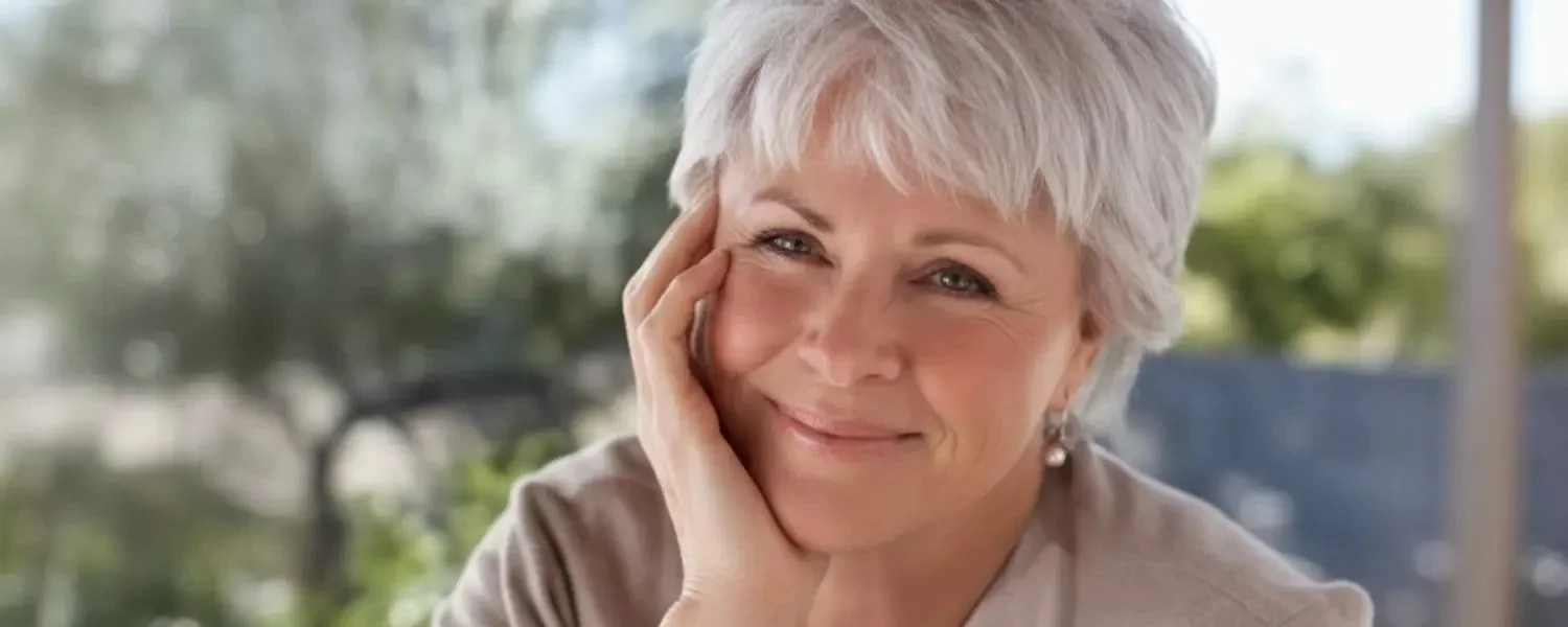 Retrato de Byron Katie sonriendo al aire libre con la mano en el rostro.
