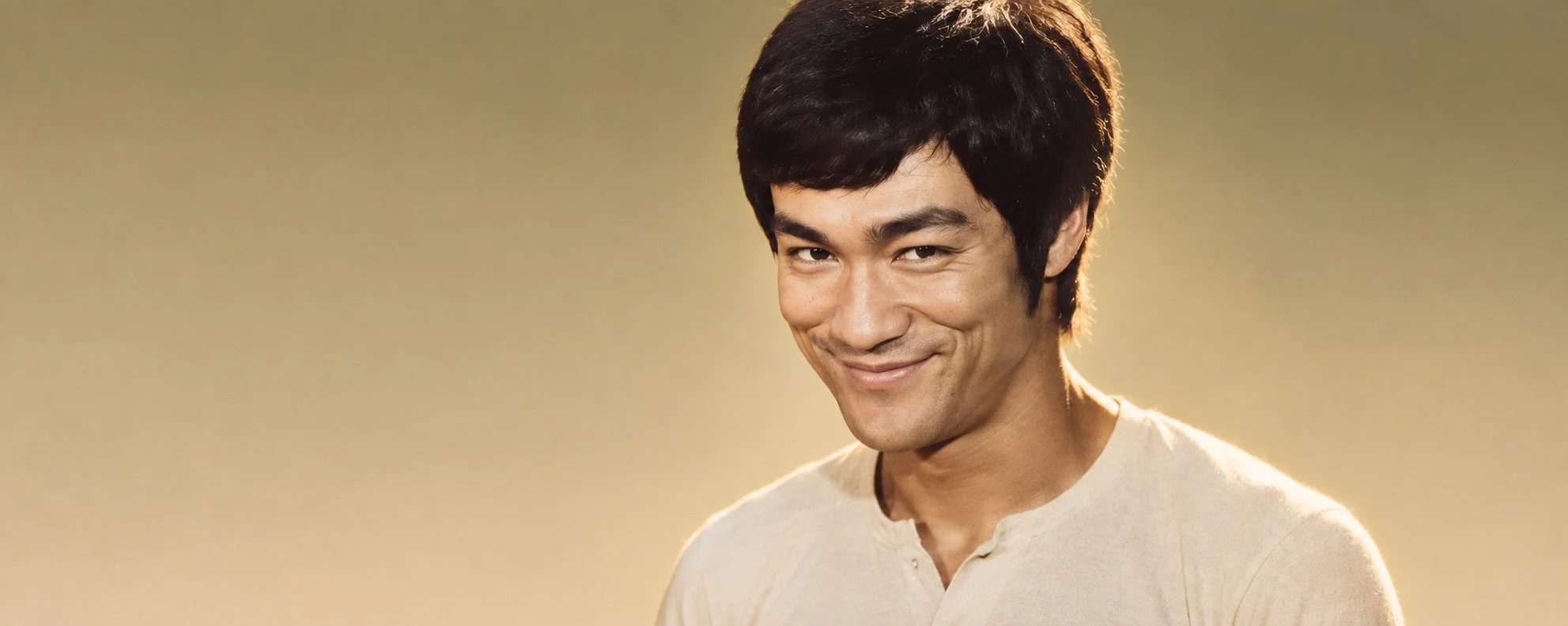 Retrato de Bruce Lee con luz cálida sobre fondo neutro.