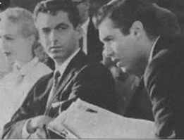 Three men and one woman seated at a table, reading documents, in black and white.
