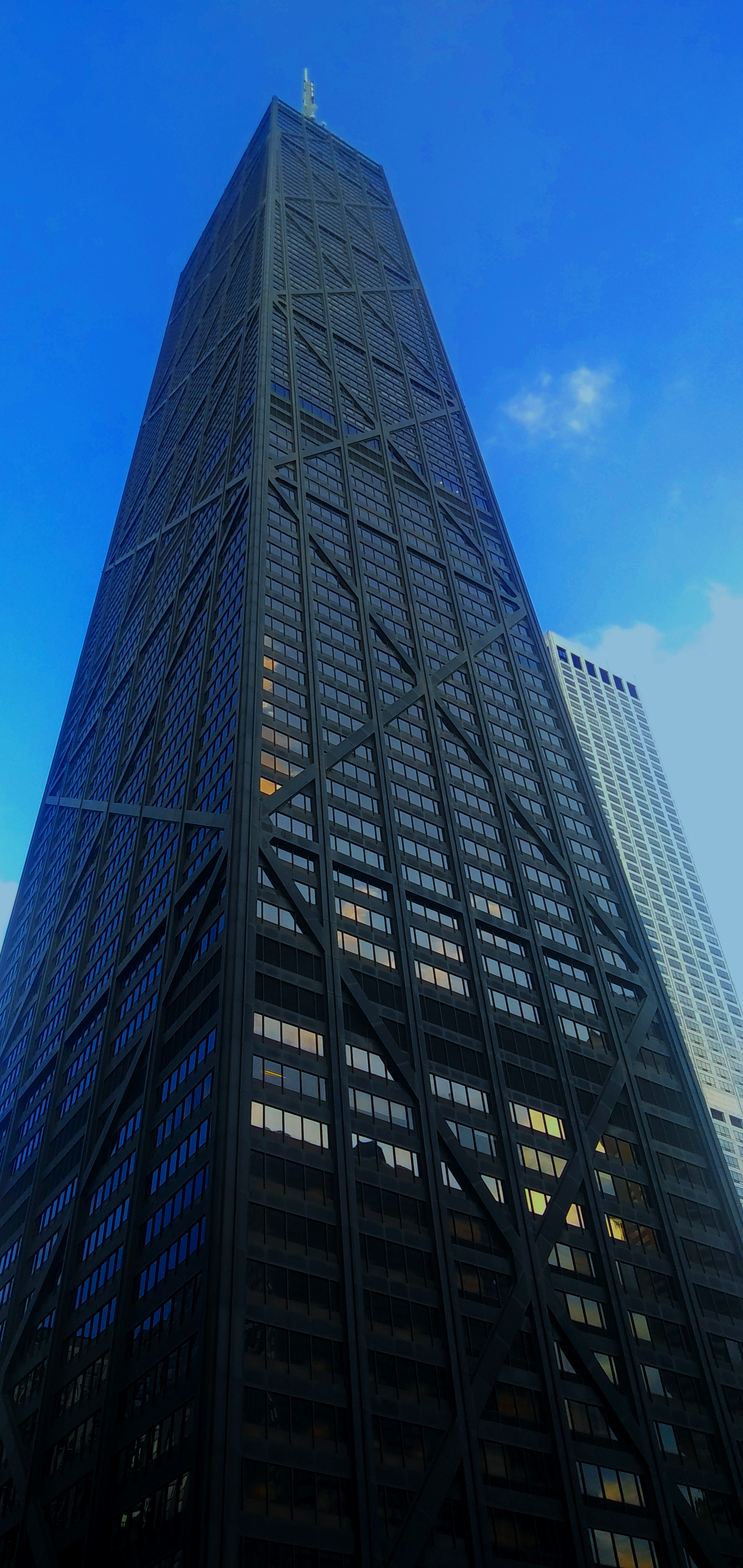 Looking up at a tall skyscraper with a crisscross architectural design, against a clear blue sky.