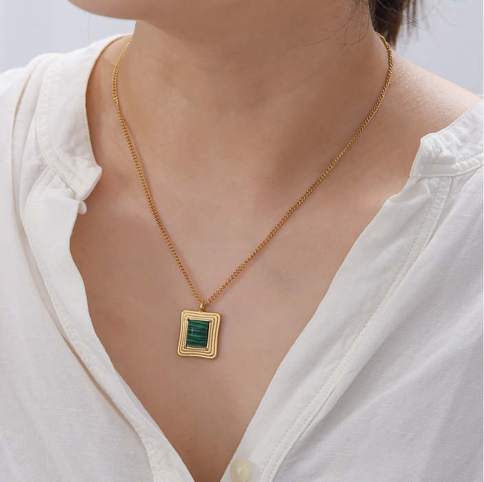 Woman wearing a gold necklace with a rectangular green stone pendant, paired with a white blouse.