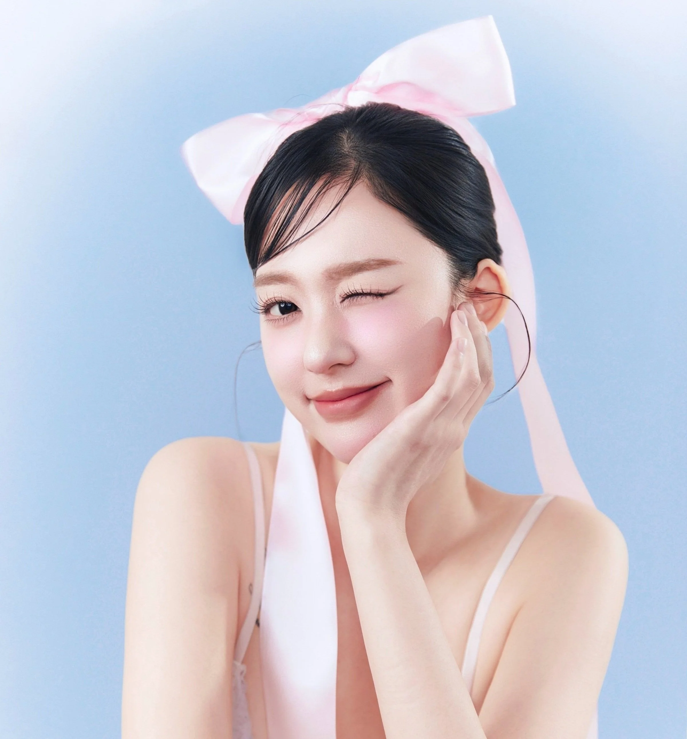 Woman with pink bow hair accessory winking against blue background.