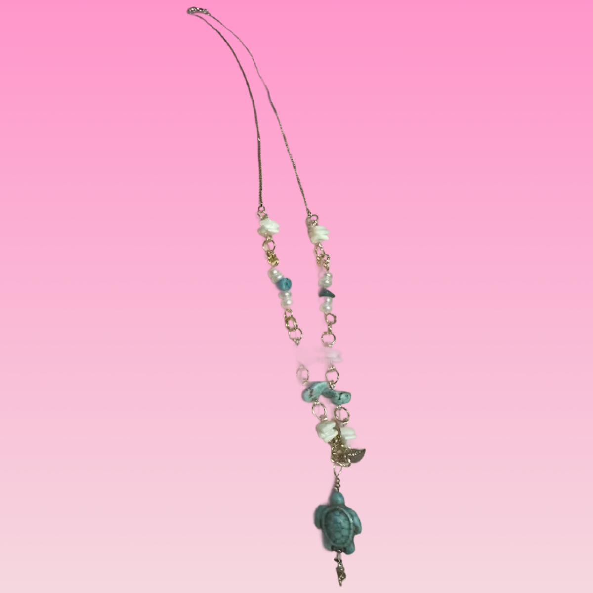 Necklace with turquoise turtle pendant and various beads, photographed on pink background.