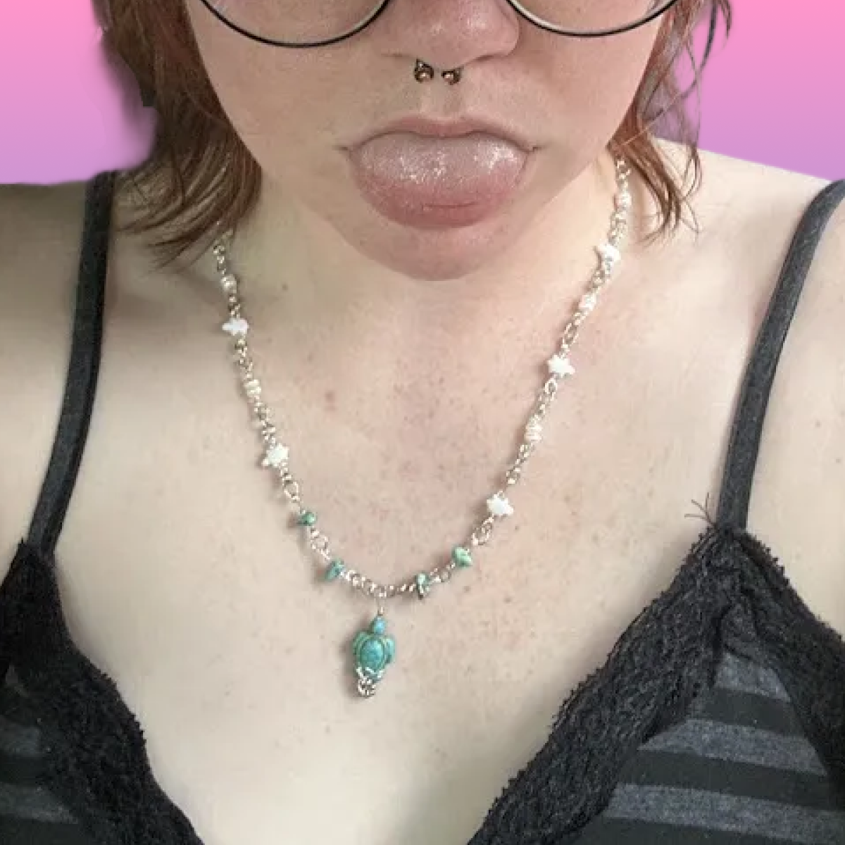 A woman with glasses, a septum piercing, and glittery lips, wearing a black lace-trimmed top and a beaded necklace with turquoise pendants.