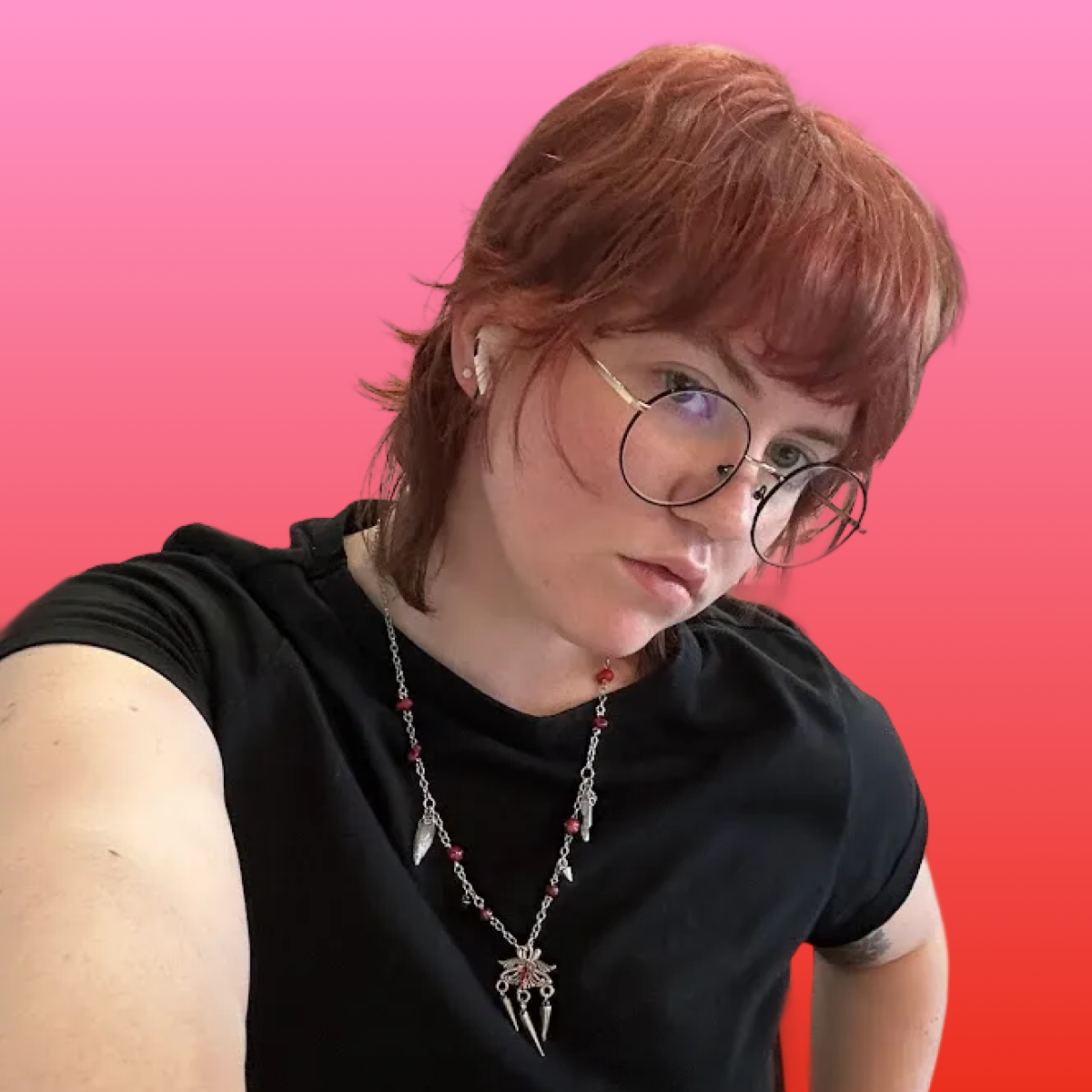 A young woman with red hair, glasses, and piercings, wearing a black shirt and a necklace with various charms, against a pink background.