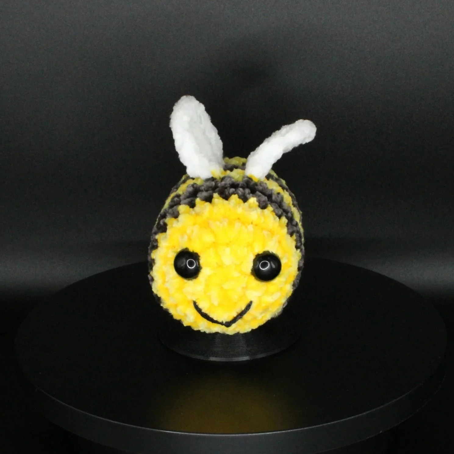 A cupcake decorated as a cute bee with a yellow face, black eyes, a smile, white antennae, and black and yellow stripes.