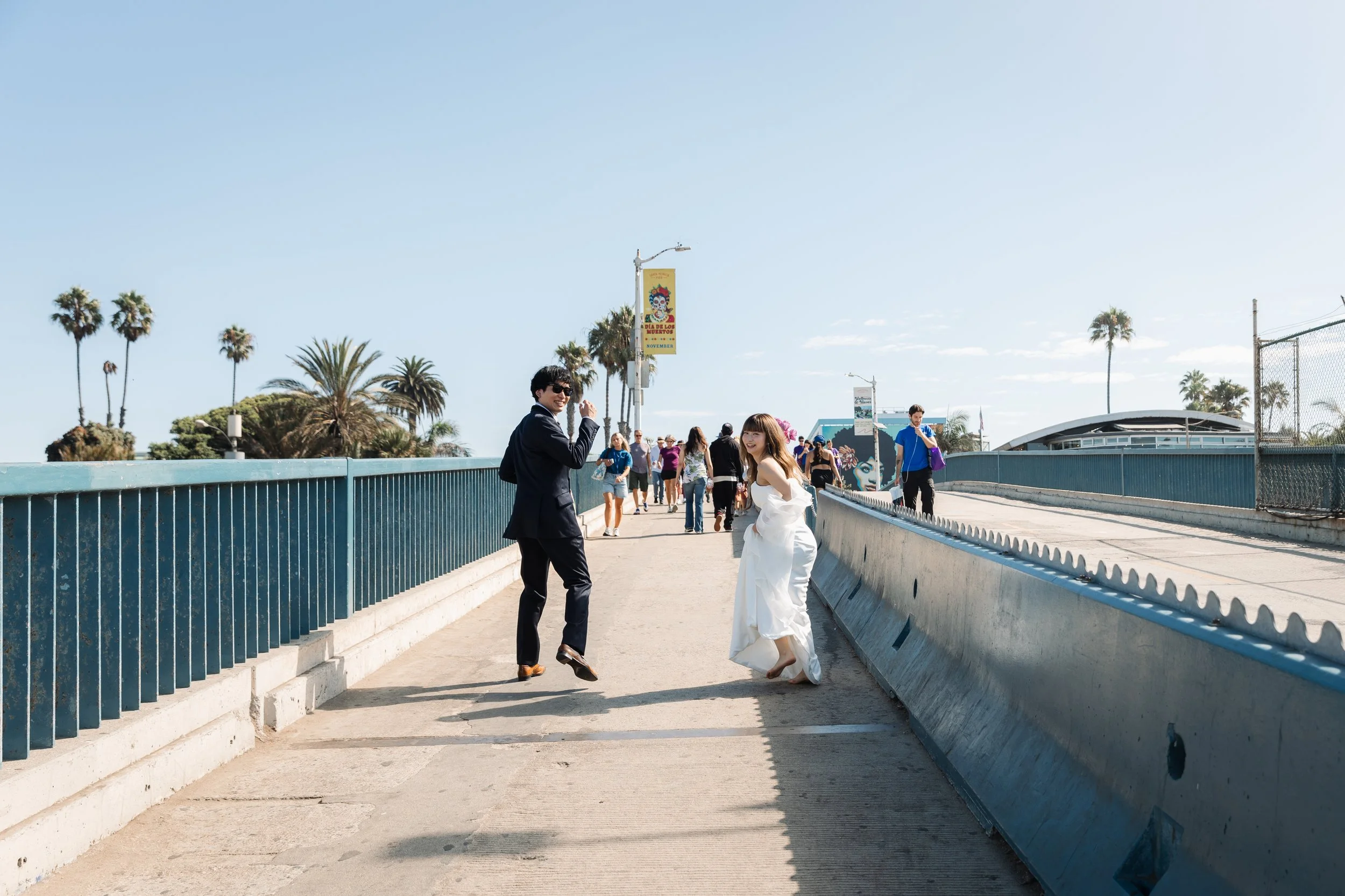 ロサンゼルス・サンタモニカで結婚写真を撮るカップルと観光客が歩いている海辺の橋の風景