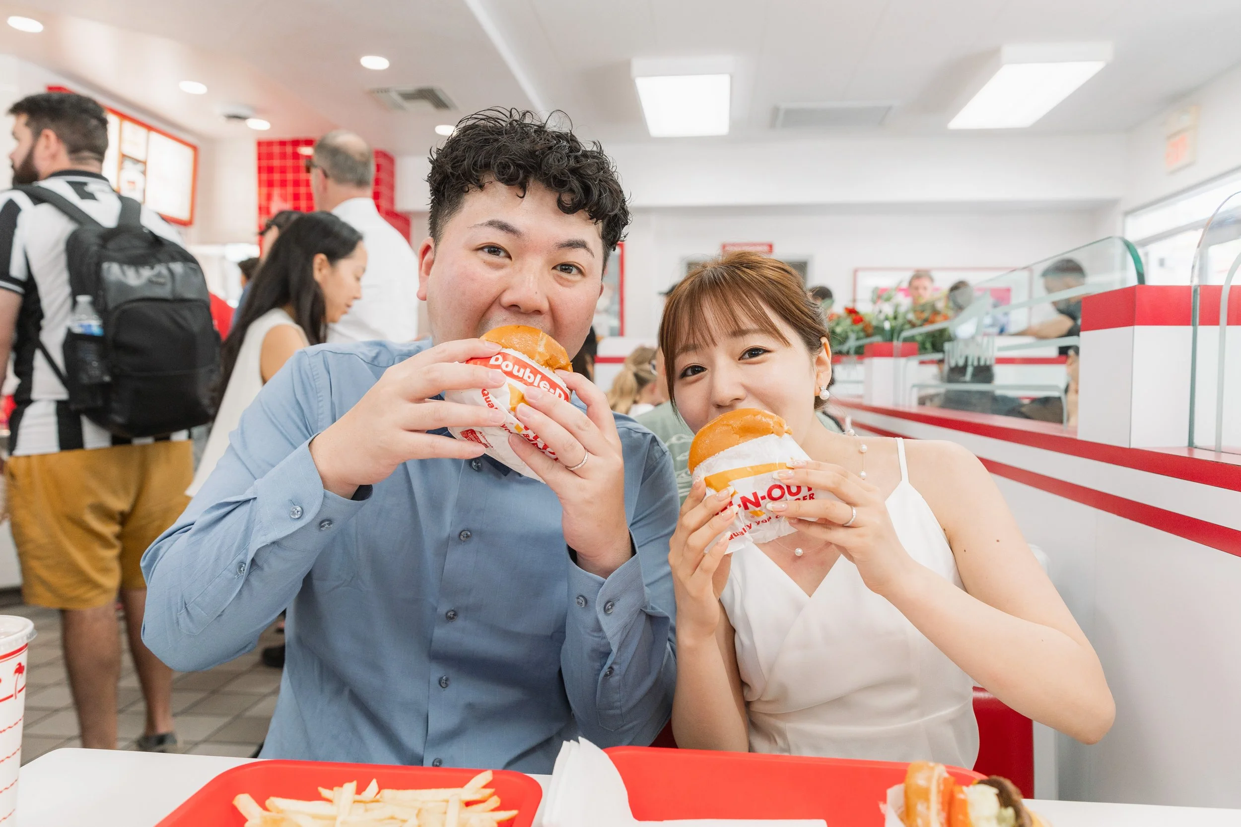 ハンバーガーを持って食べる若いカップルの写真。店内で楽しそうに笑っている。