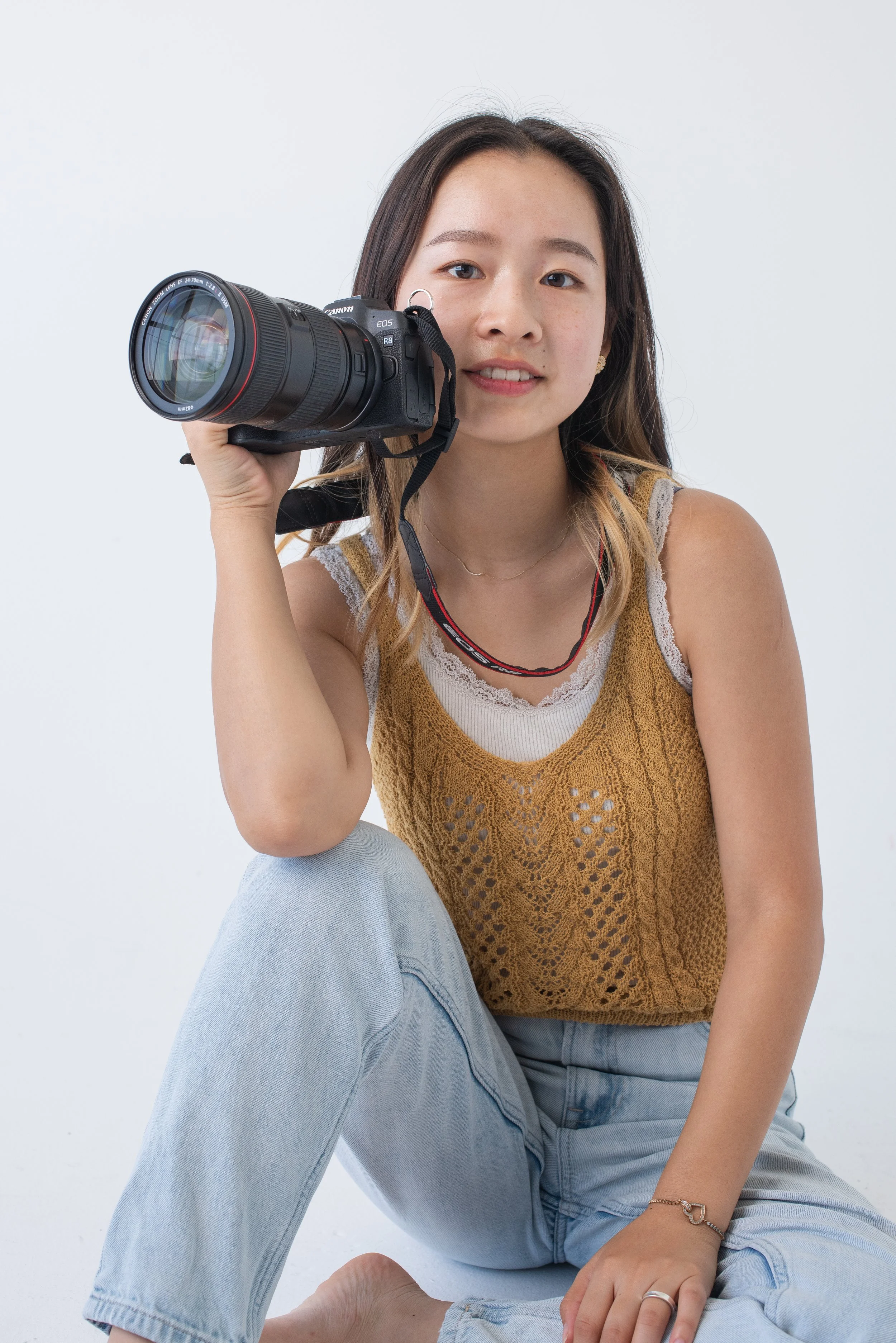 カメラを持った若い女性が座っている。白い背景。