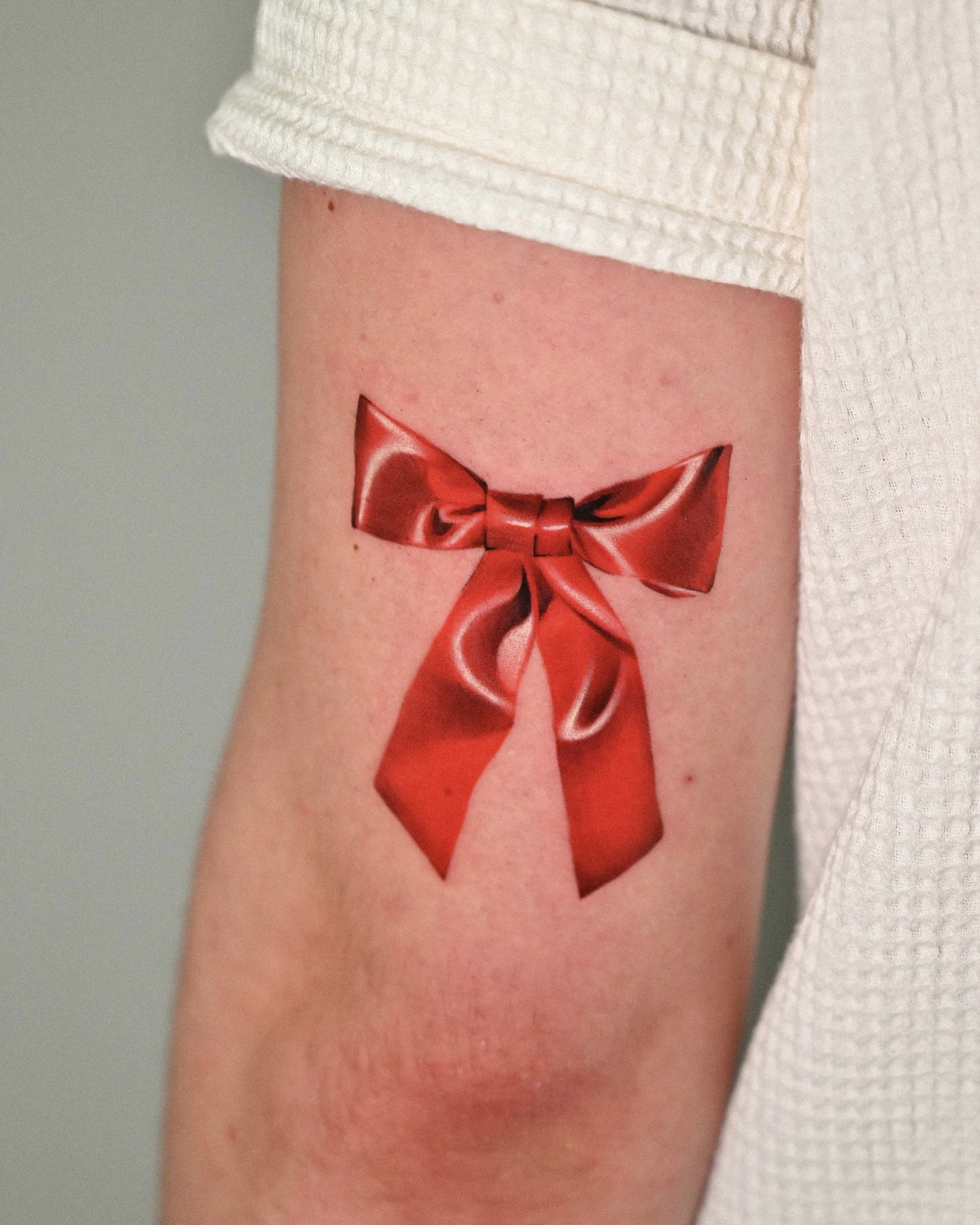 Red bow upper arm tattoo by Seattle tattoo artist Megink.