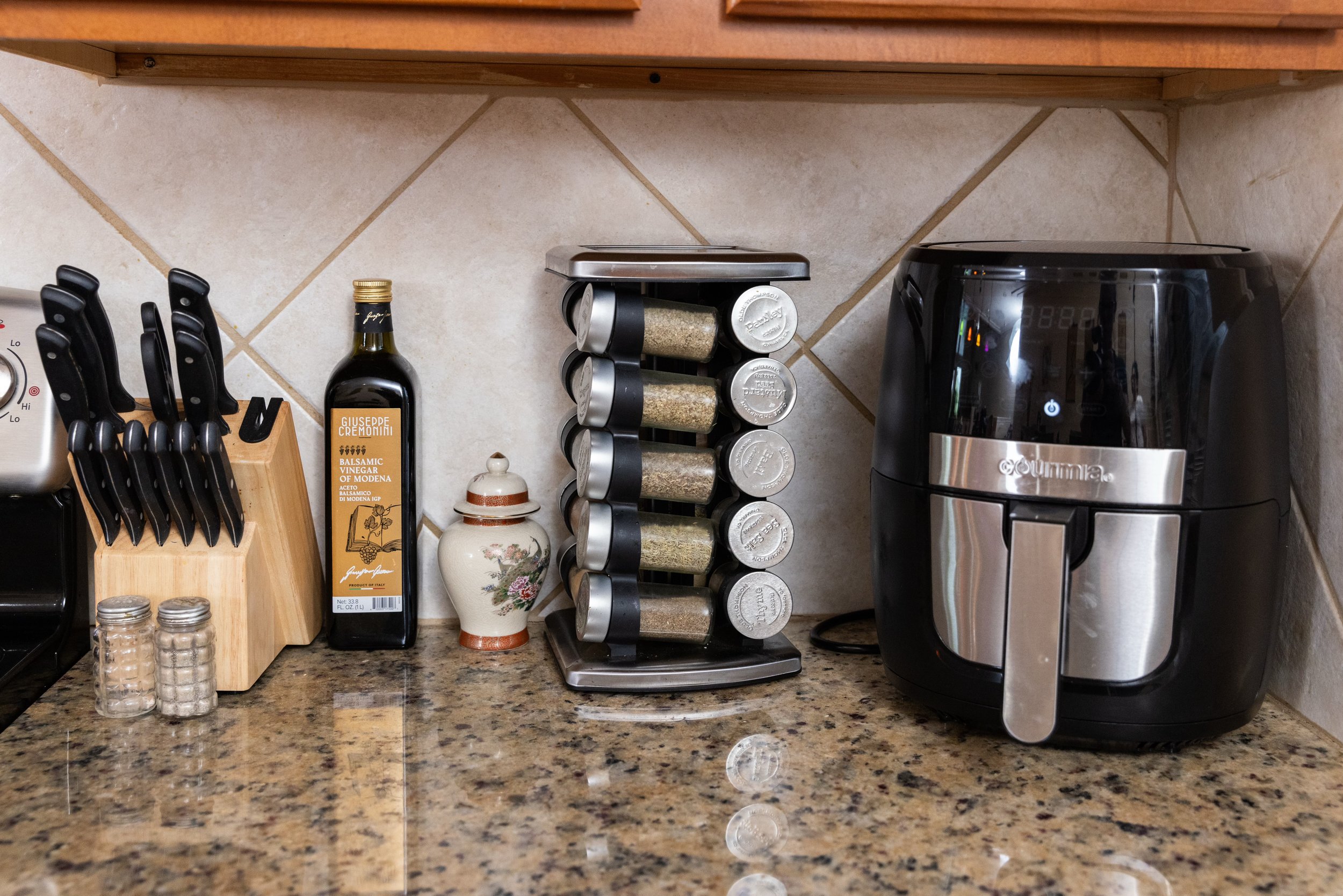Kitchen countertop with knife block, balsamic vinegar bottle, spice rack, and air fryer.