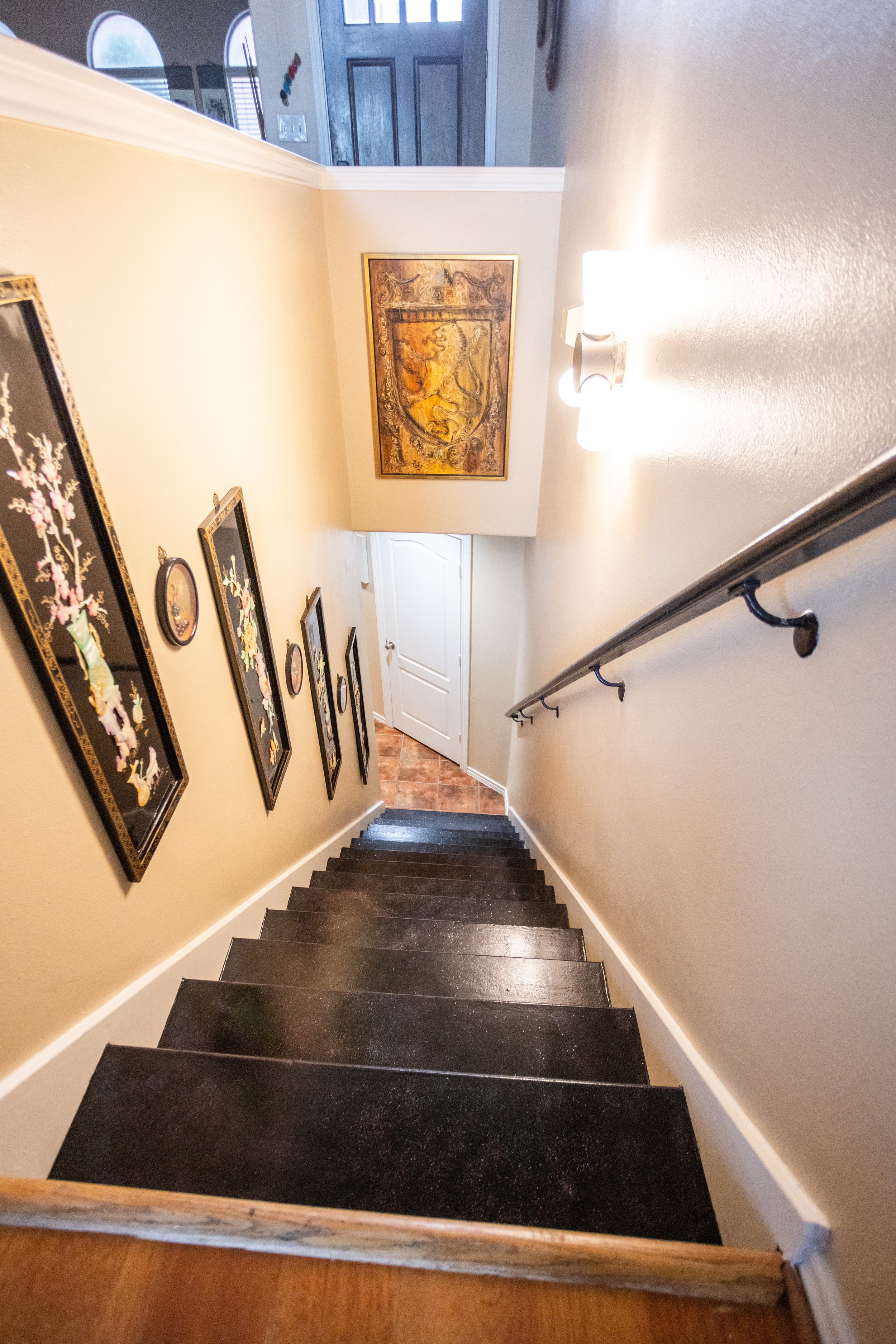 Interior staircase with wooden steps, a wall decorated with framed art, a handrail, and a light fixture.