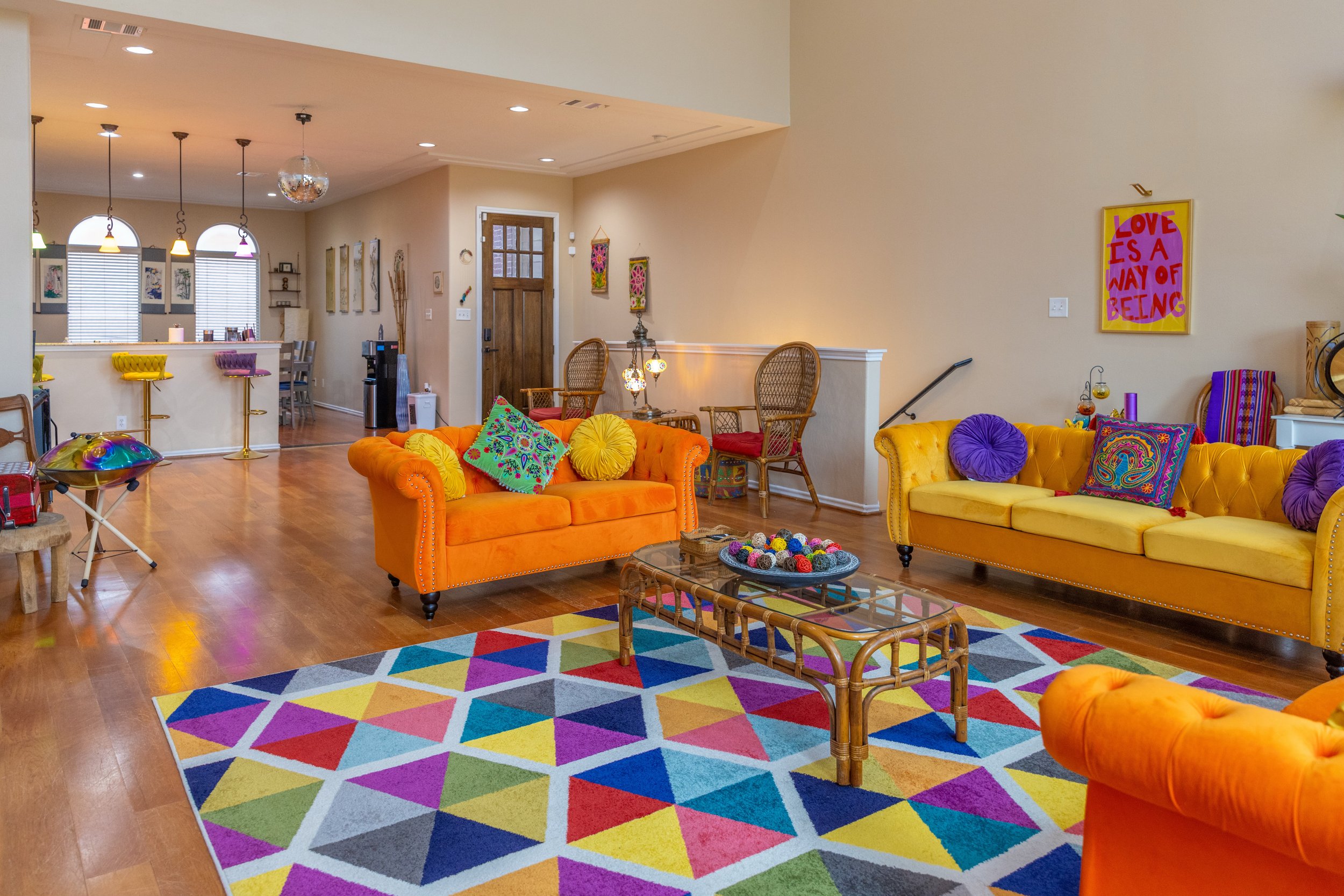 Colorful living room with vibrant orange and yellow couches, multicolored geometric rug, and eclectic decor.