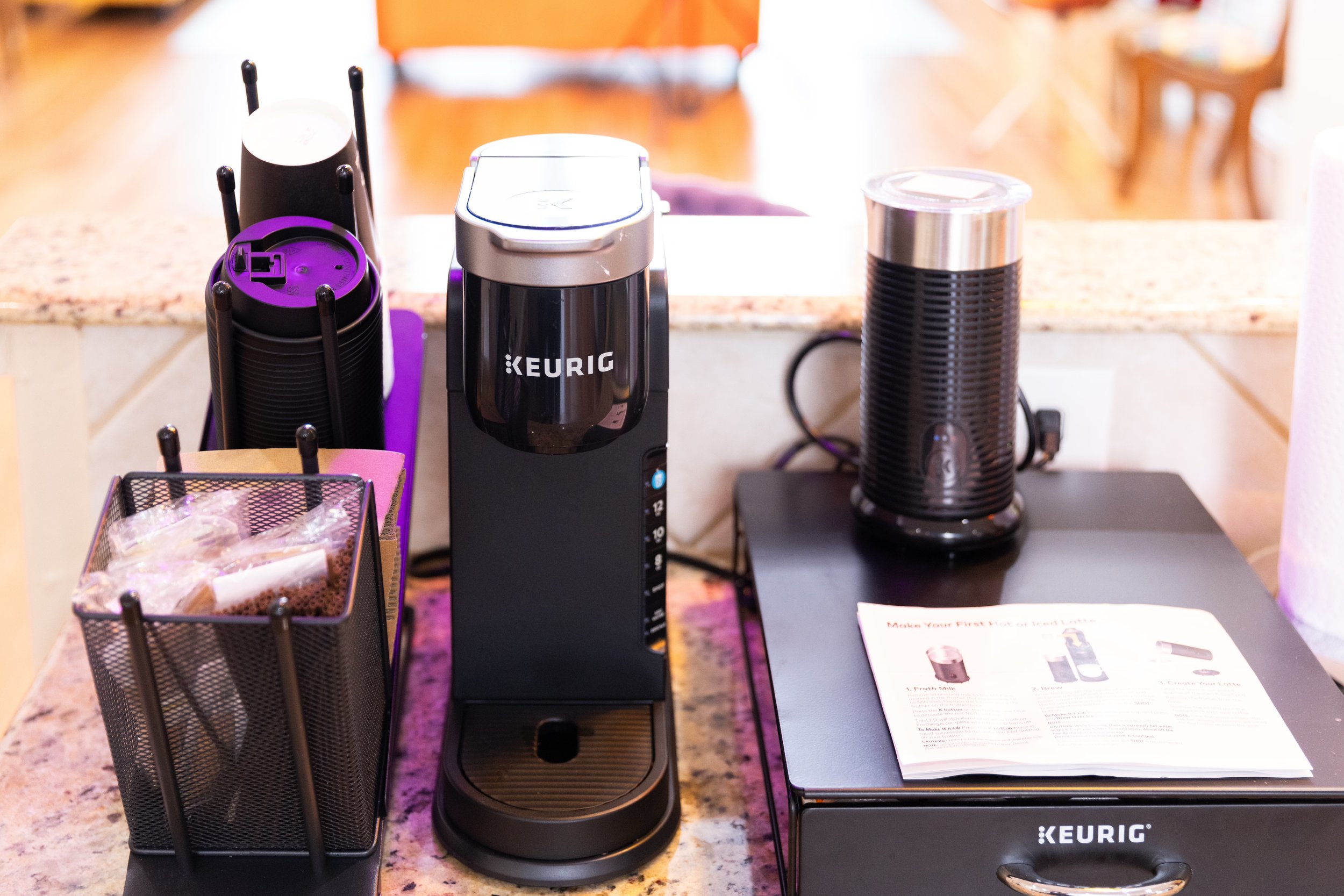 Keurig coffee maker setup with pods on a countertop, accompanied by a milk frother and an instruction manual.
