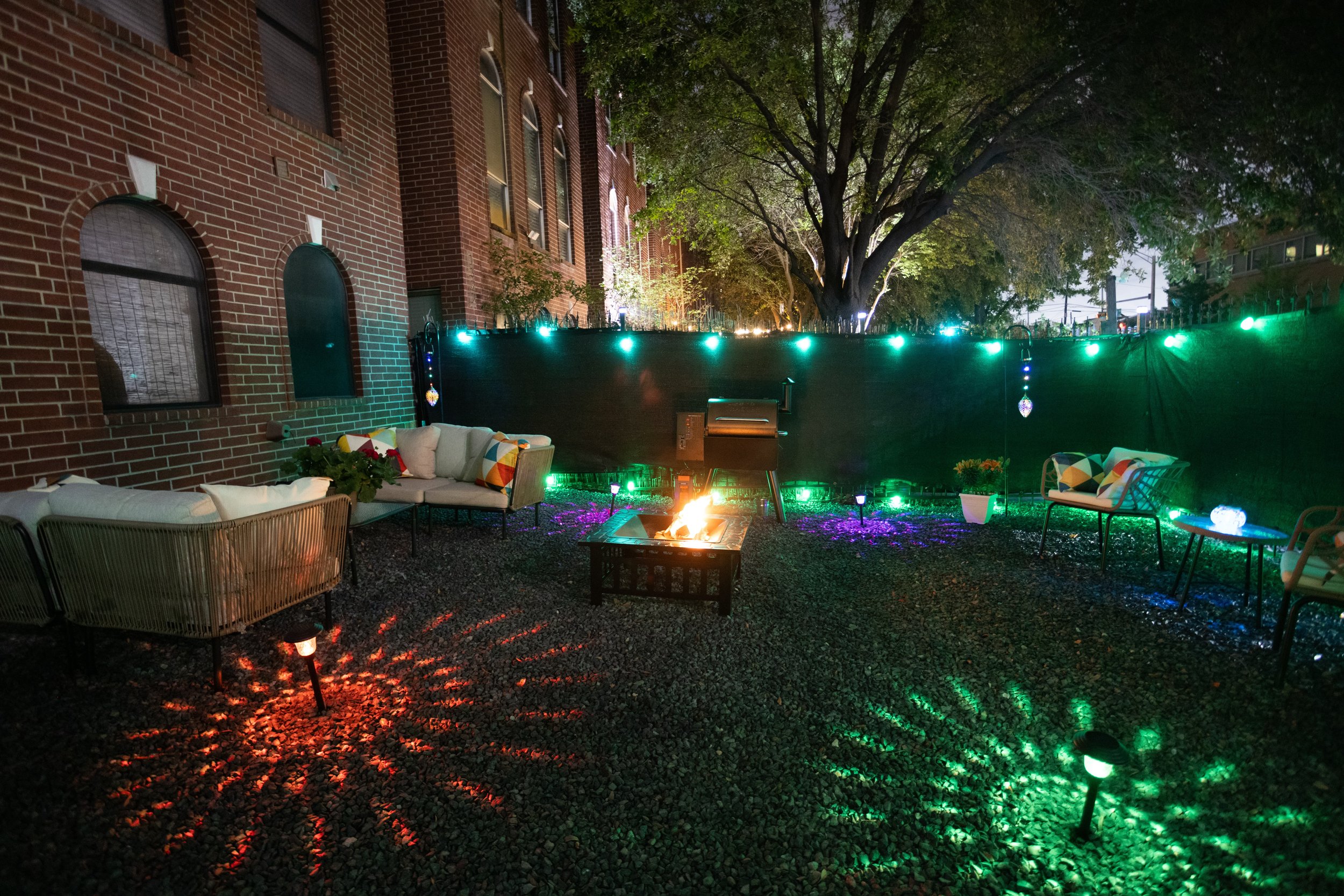 Outdoor patio with brick wall, seating area, fire pit, and colorful string lights.