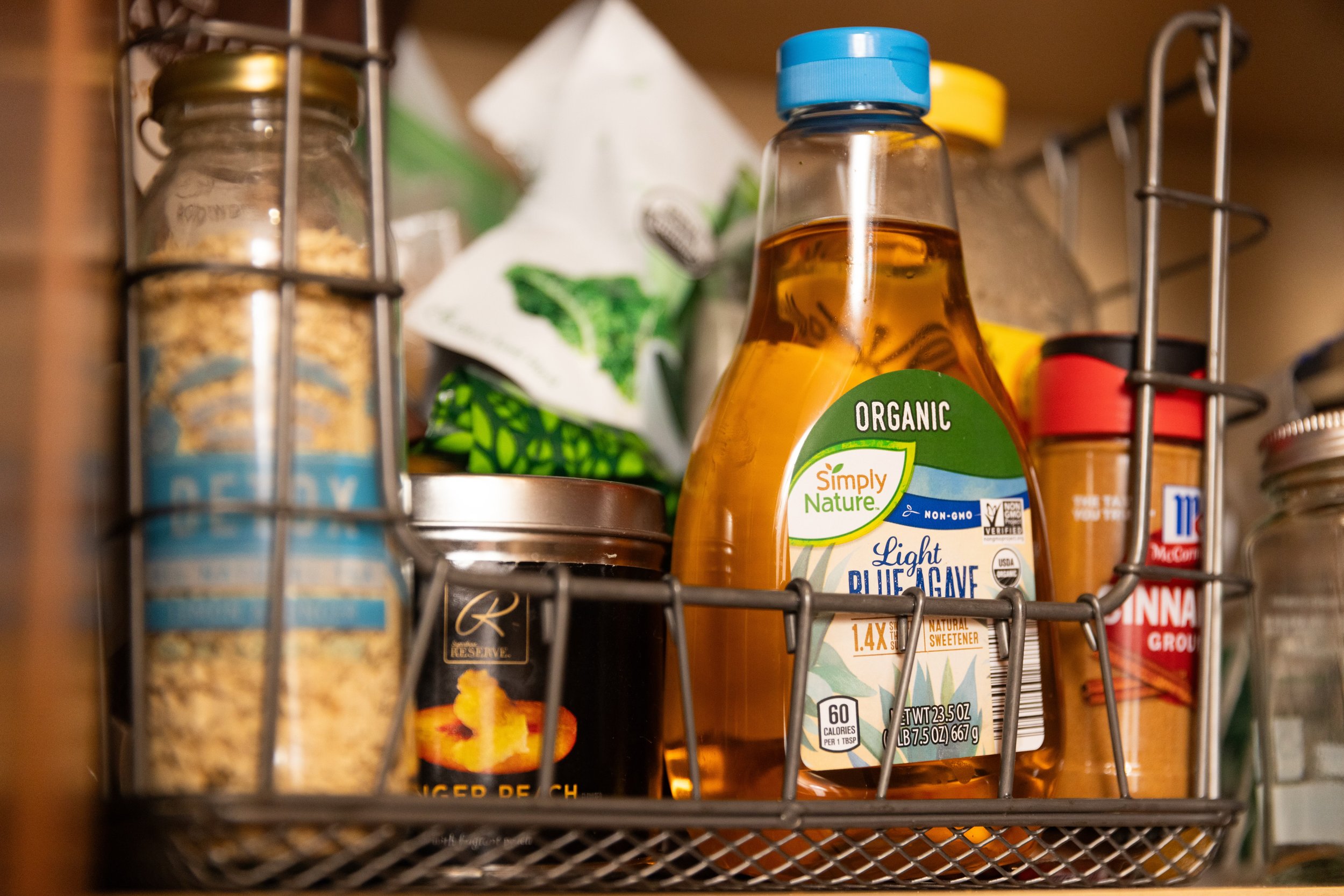 Pantry shelf with organic agave syrup, ground cinnamon, and various food jars.