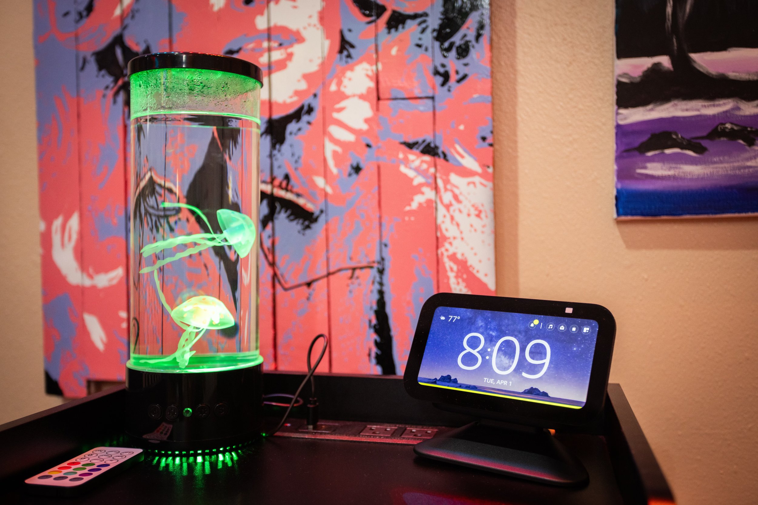 A jellyfish lamp emitting green light next to a smart display showing 8:09, set against a colorful wall art background.