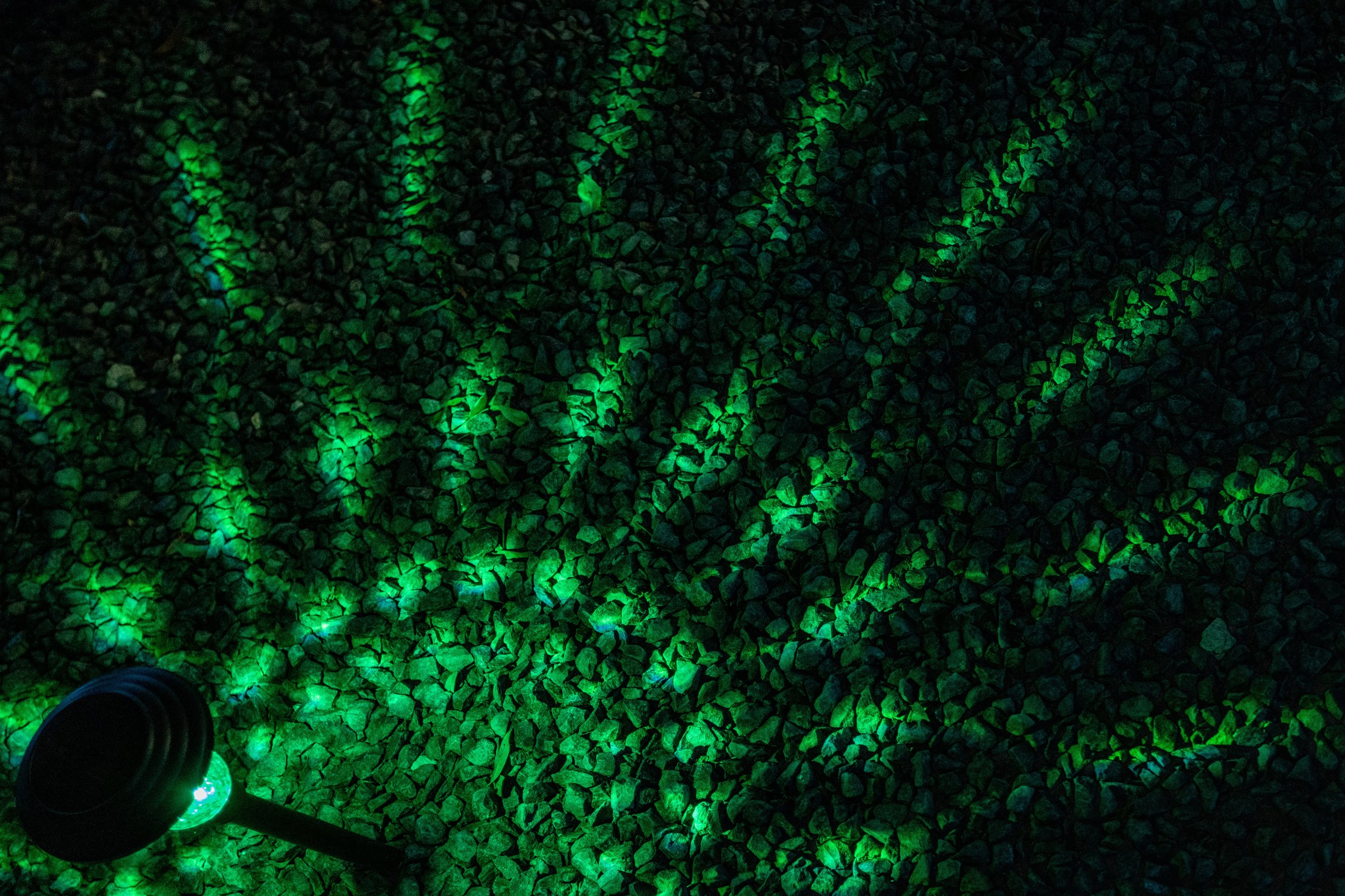 Green LED ground light casting patterns on rocks at night