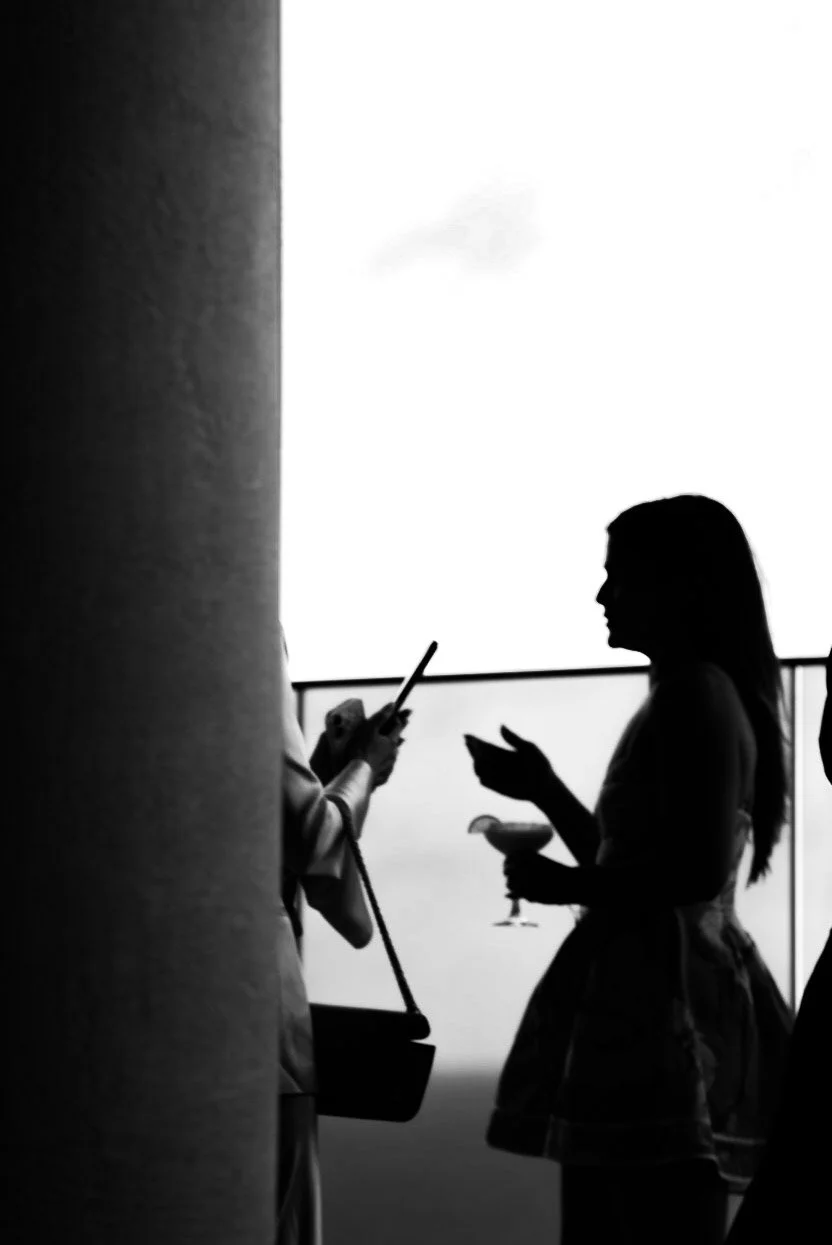 Silhouettes of two women, one holding a drink, standing and using her phone