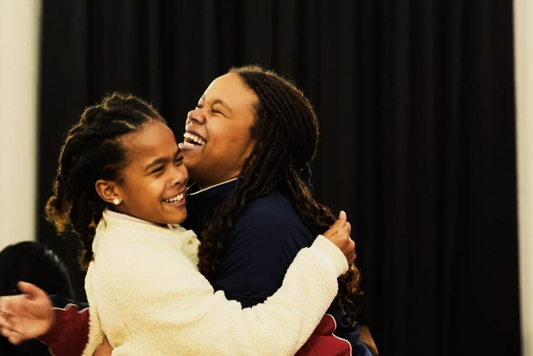 Two women hugging and smiling at each other in an indoor setting.