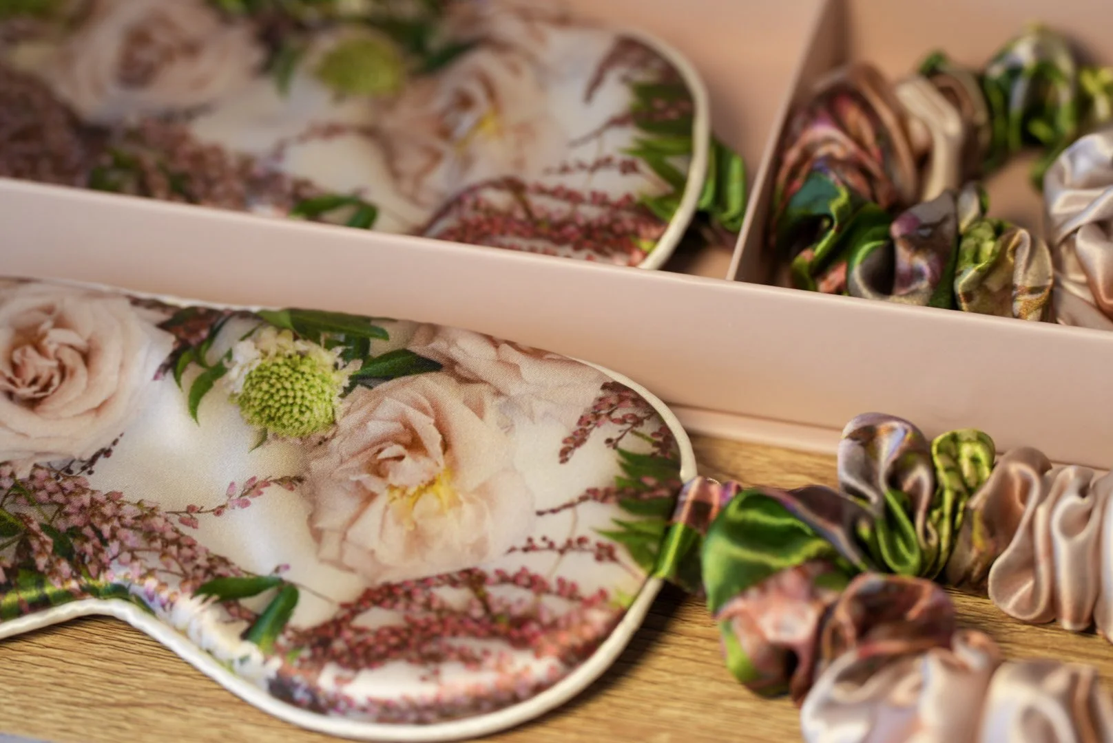 A pink box containing floral-patterned satin slippers and silk scrunchies with multicolored floral designs.