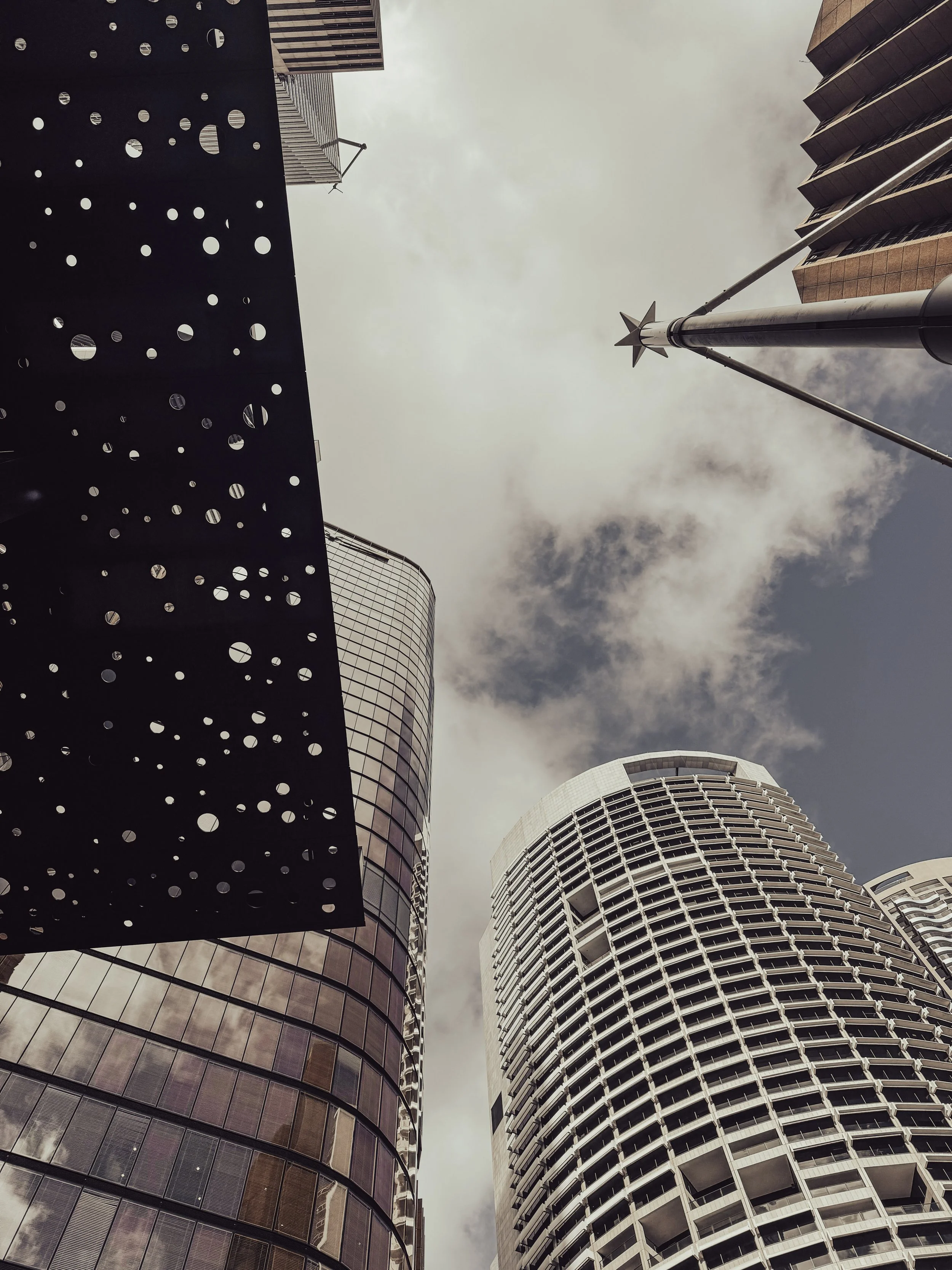 A low-angle view of modern skyscrapers with glass facades and a sky with clouds.