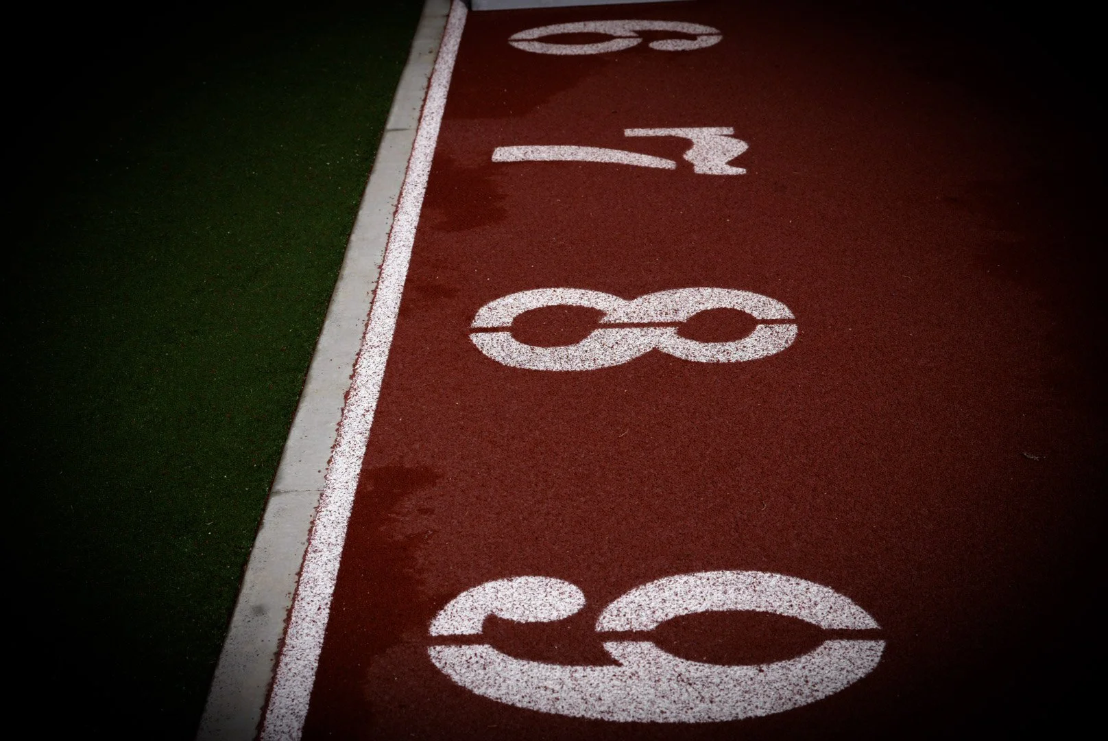 Close-up of a red running track with white lane markings and lane numbers 3, 4, 5, 6, 7, and 8.