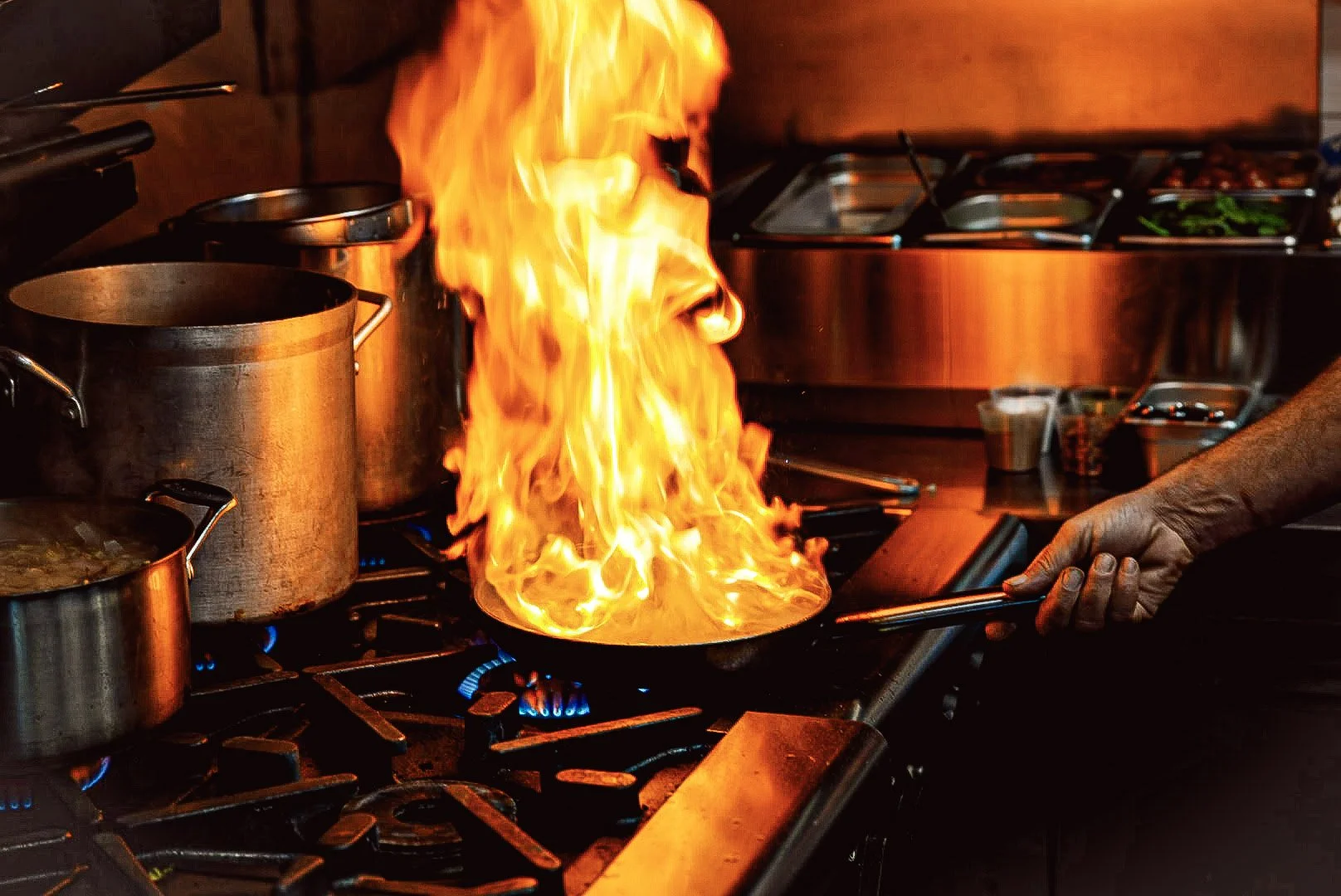 A chef is cooking on a stove with flames rising from the pan.