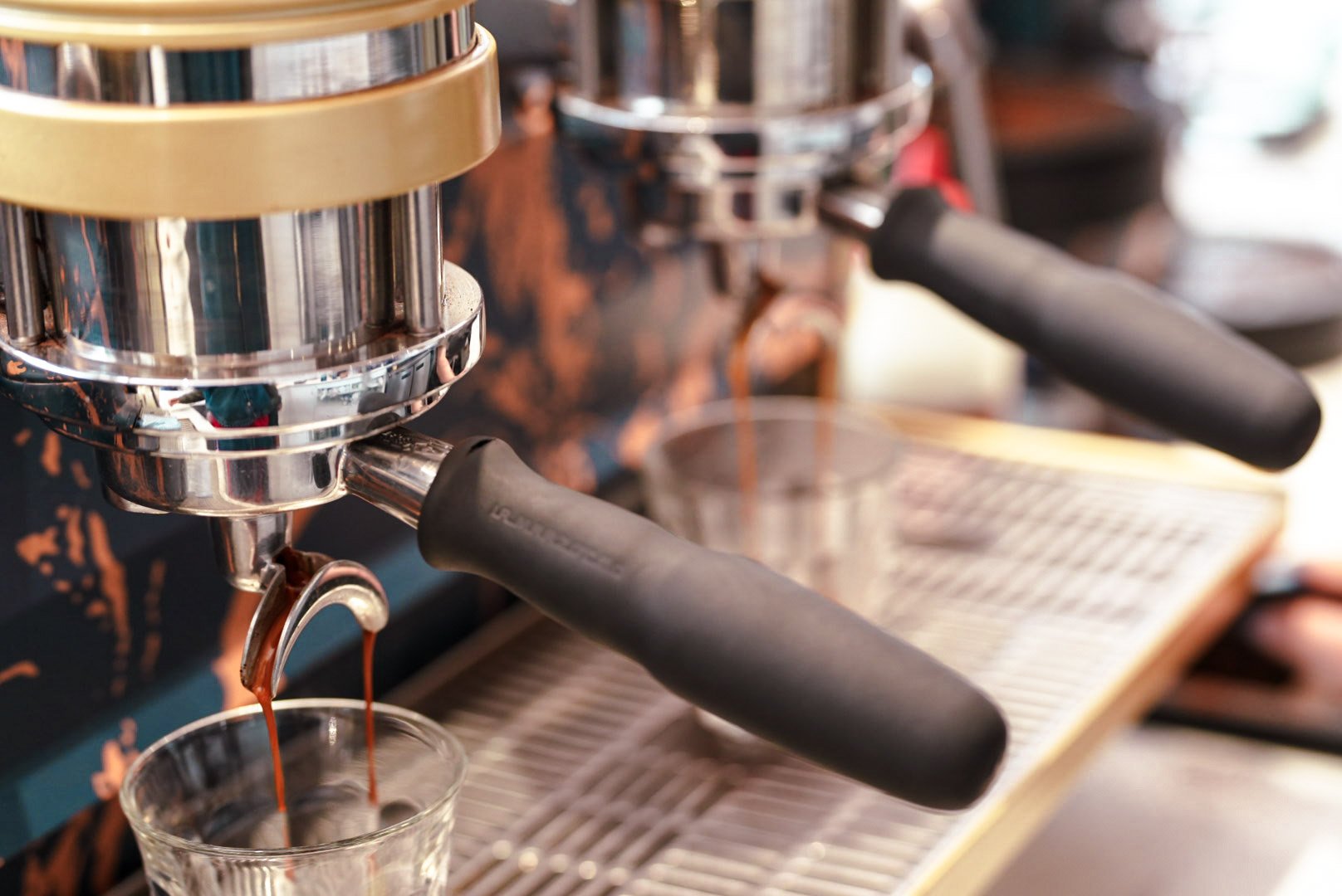 Close-up of a espresso machine dispensing coffee into a glass, with a portafilter attached and a second portafilter in the background.