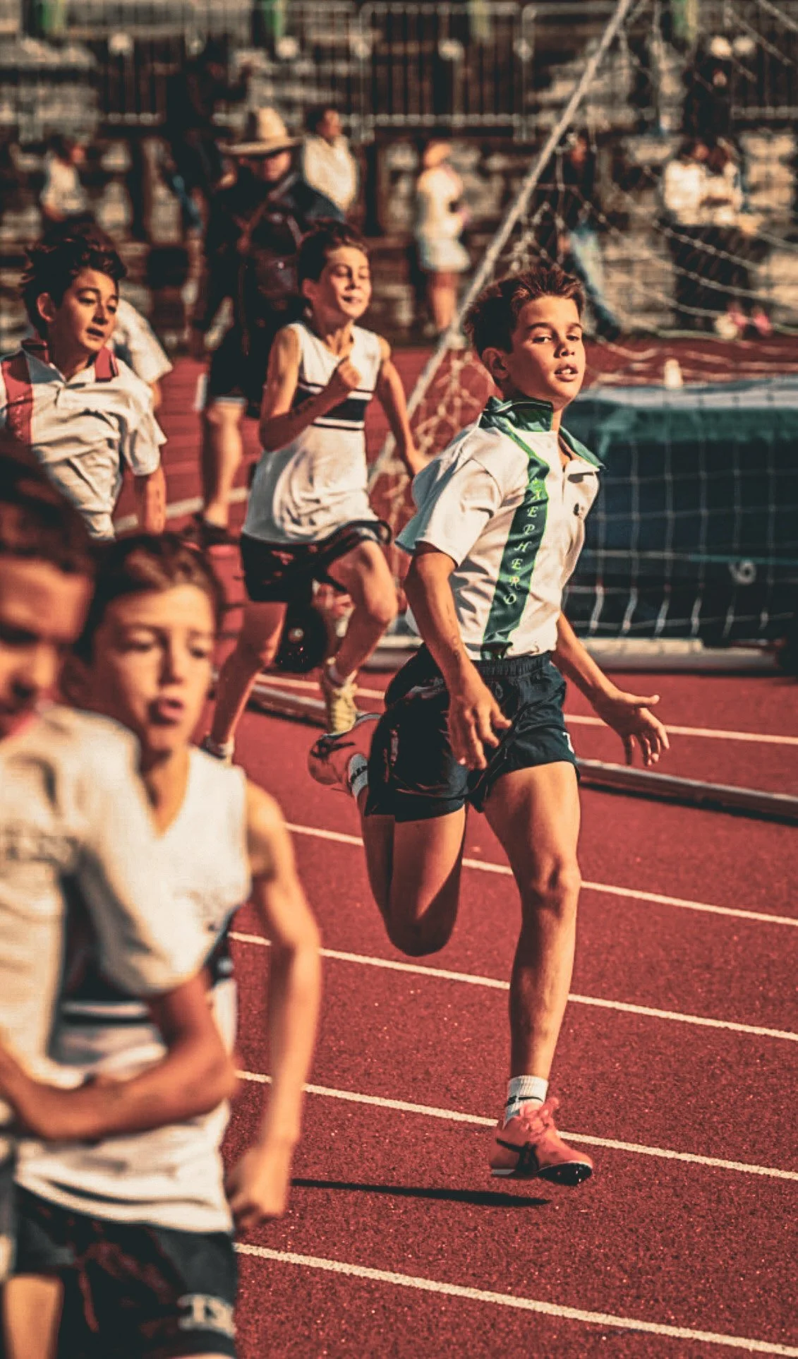 Young boys running on a track during a race at a stadium.