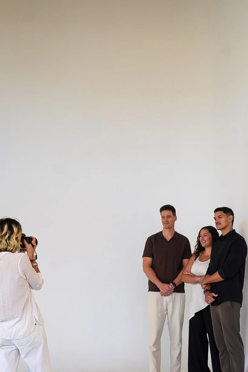 A group of three diverse people posing for a photograph against a plain white wall, while a photographer with a camera captures the moment.
