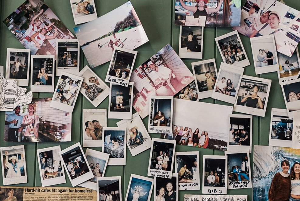 Collection of printed photographs displayed on a green wall, capturing various moments of people at parties, beaches, and gatherings.