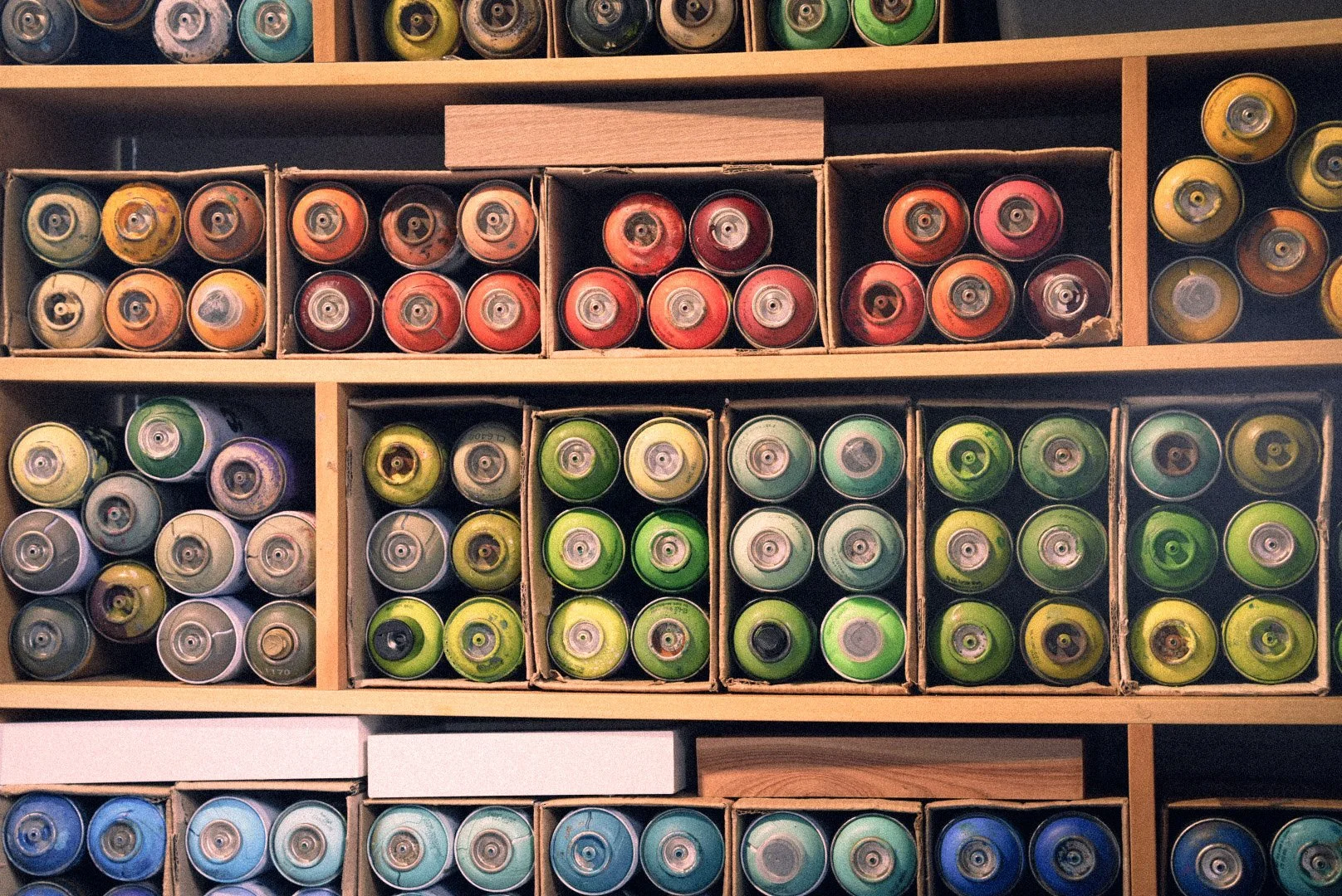 Shelves filled with spray paint cans in various colors, organized in cardboard boxes.