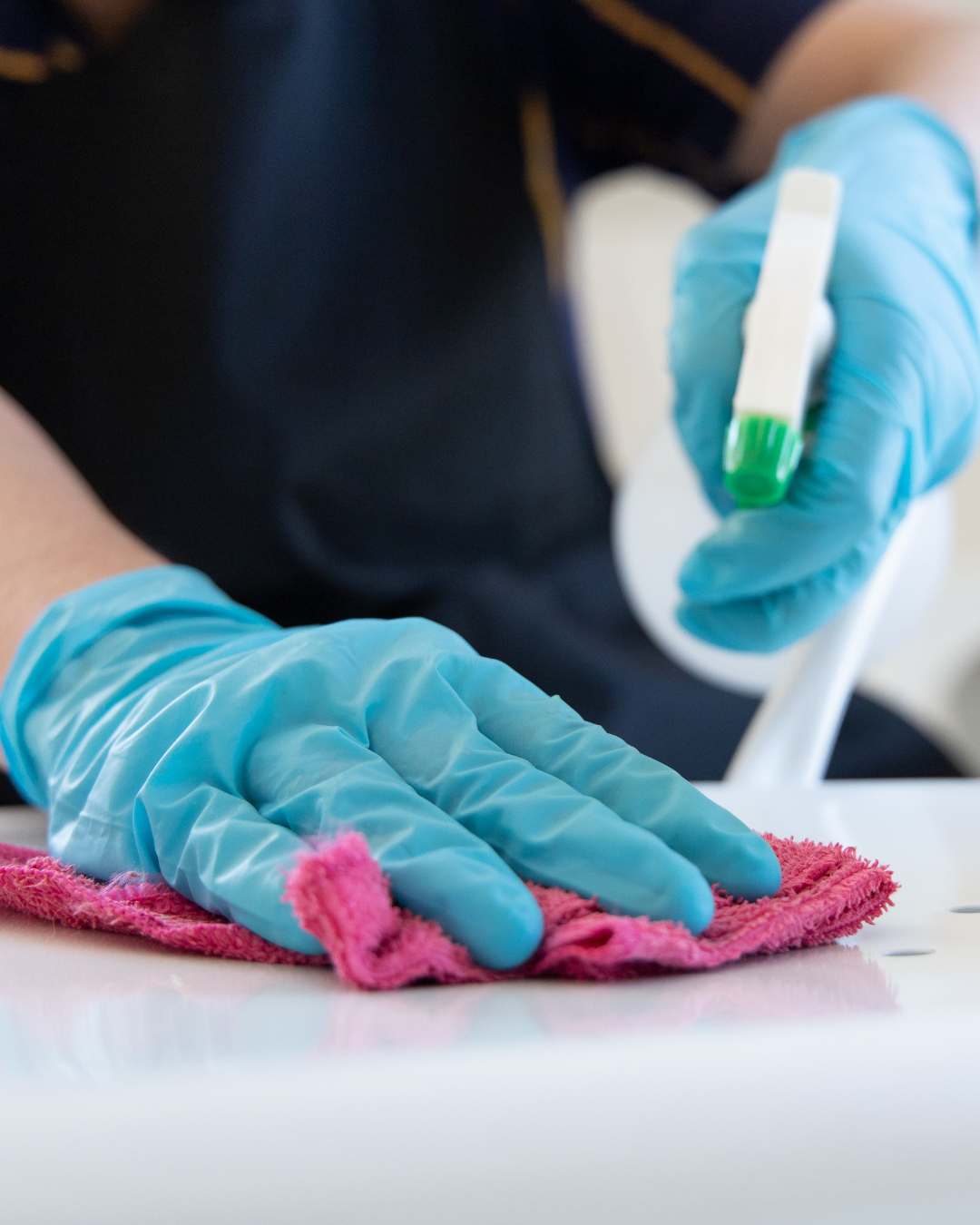 A person with gloved hands cleaning a benchtop