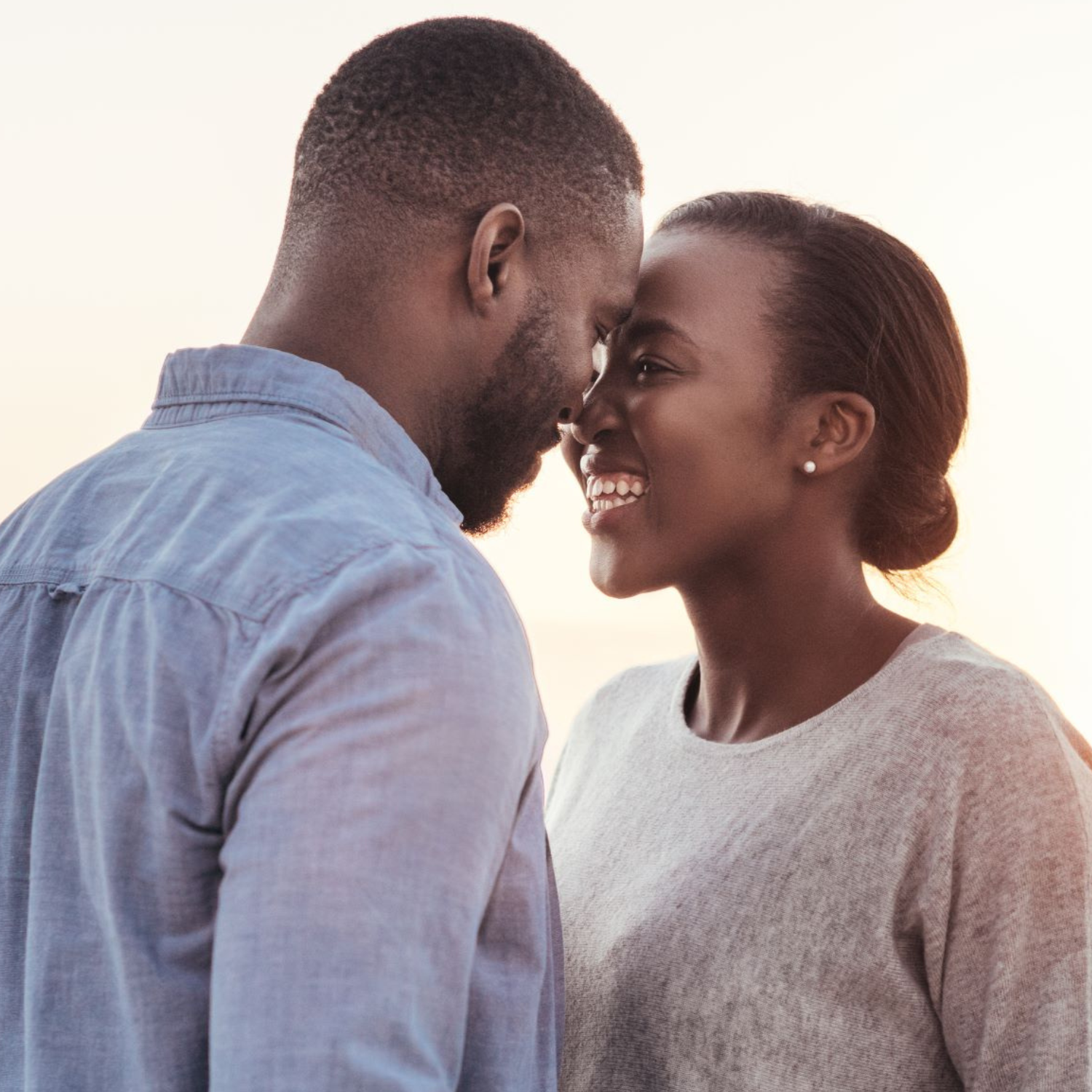 A close-up of a couple smiling and touching foreheads outdoors in soft natural lighting.