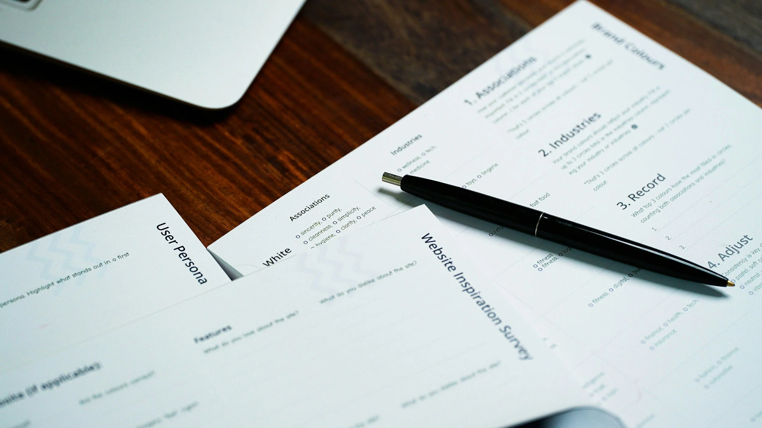 Documents and a pen on a wooden table, including a user persona sheet and a website inspiration survey.