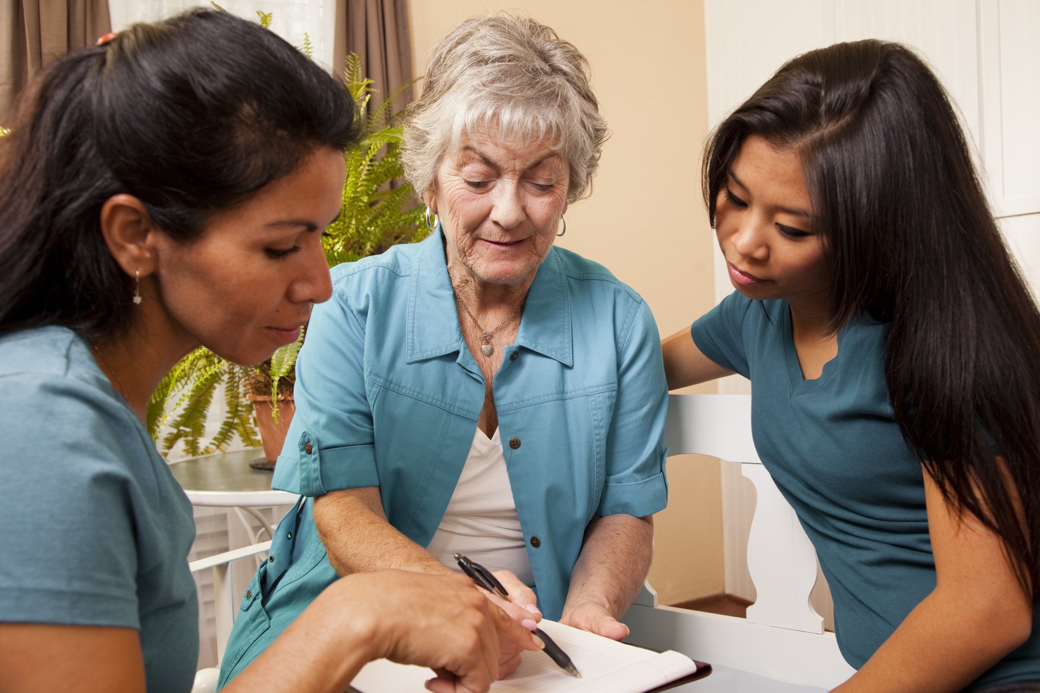 Three women, including an elderly woman and two young women, gathered around a notepad, discussing or reviewing information together in a cozy indoor setting.
