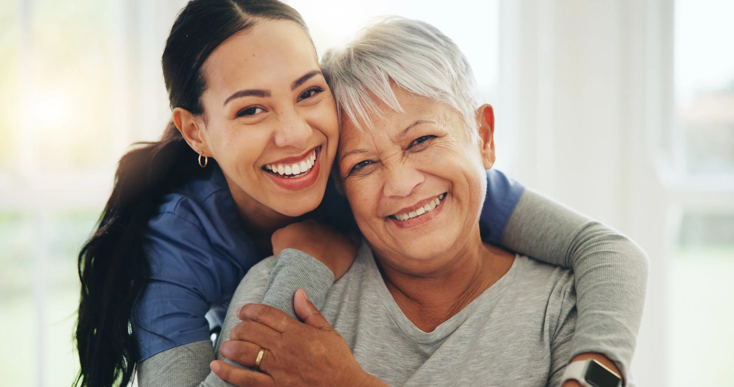 A young woman hugging an elderly woman, both smiling happily.