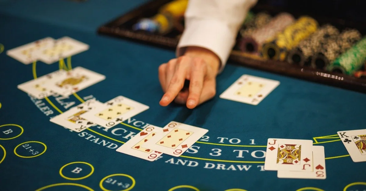 Close-up of a dealer's fingers pointing at face-up cards on a poker table. The chip rack holds many colorful chips.