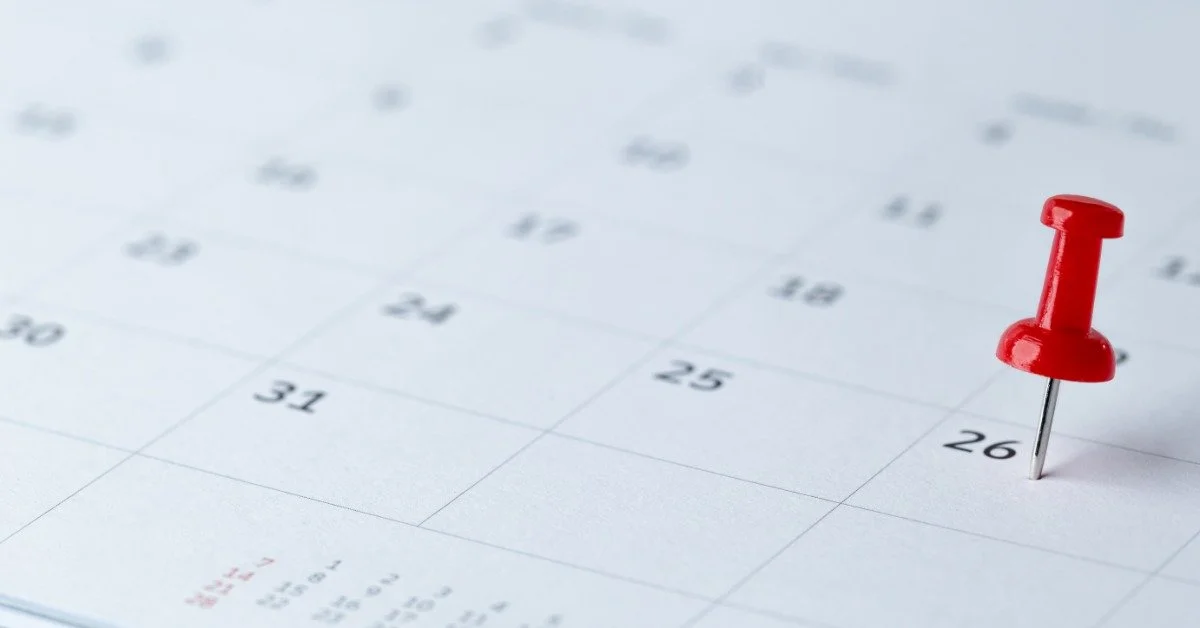A red pushpin sticks into a calendar square labeled 26. The surrounding calendar grid and dates are softly blurred.