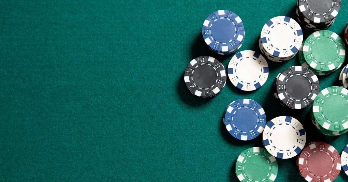 Top-down view of blue, white, green, black, and red poker chips clustered on the right side of a green felt surface.