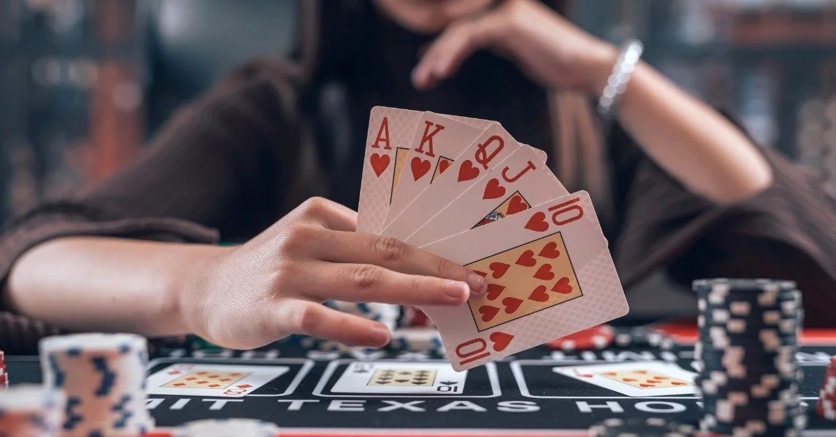 A person shows their fanned-out playing cards, revealing a royal flush. Stacks of poker chips are on the felt table.
