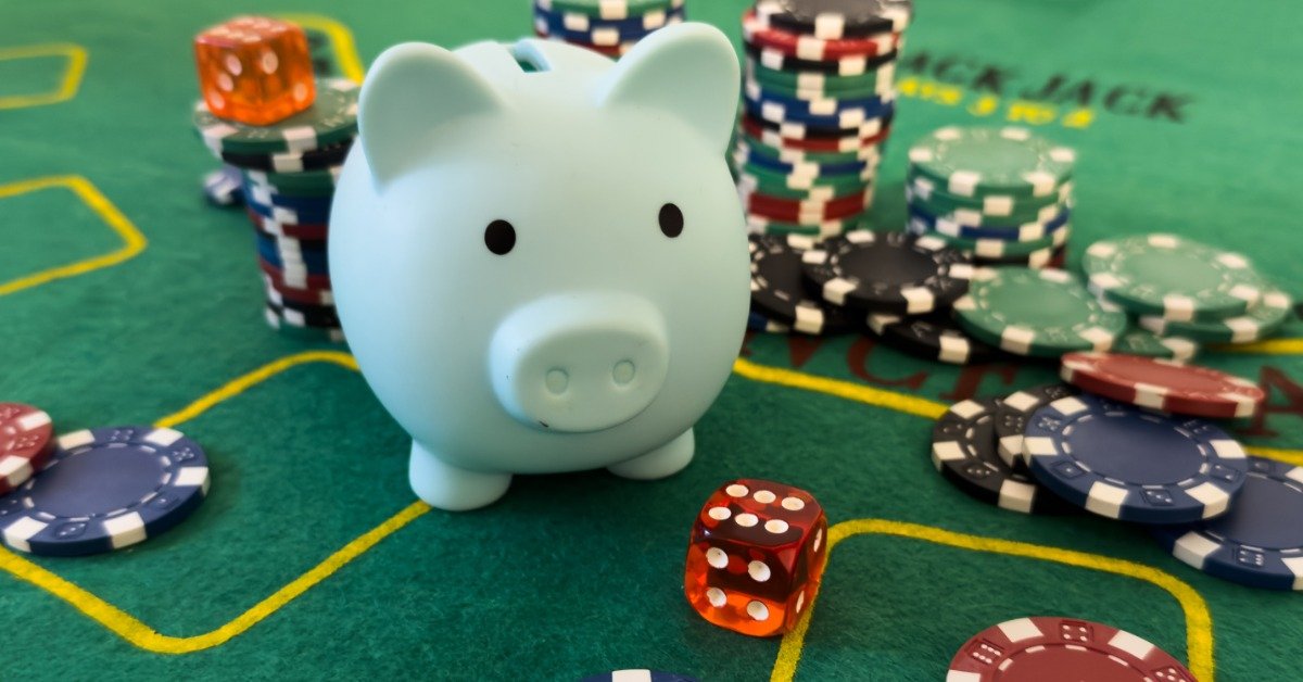 A pale blue piggy bank sits on a green casino table surrounded by multicolored poker chips and two translucent dice.