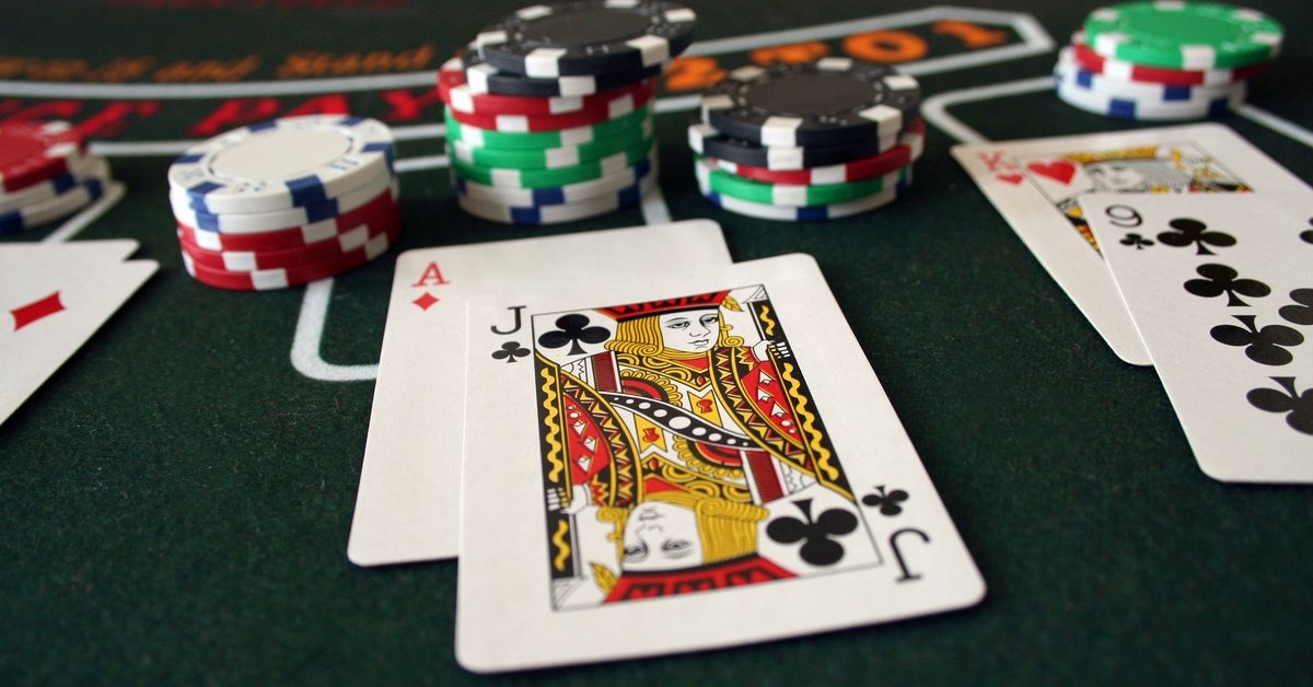 A green felt blackjack table with cards facing up and neat stacks of multicolored casino chips arranged across the surface.