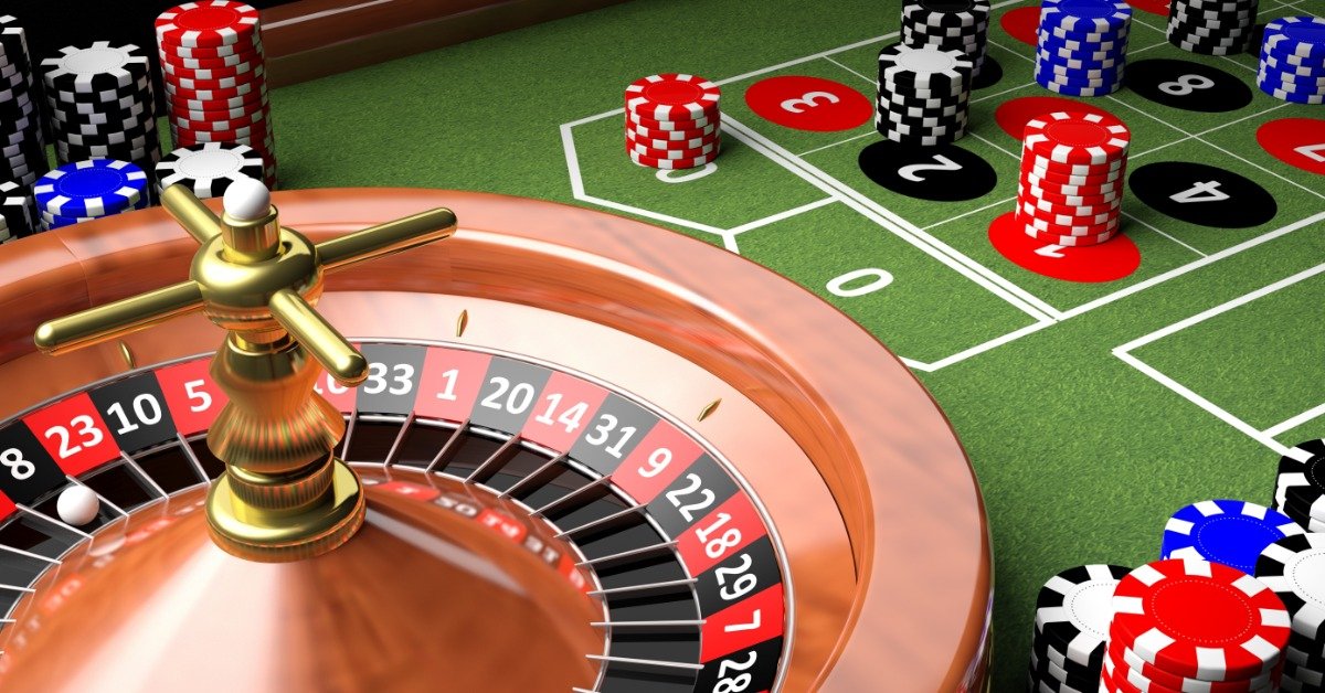 A wooden roulette wheel sits on a green roulette table next to poker chips. A small white ball is in one wheel pocket.