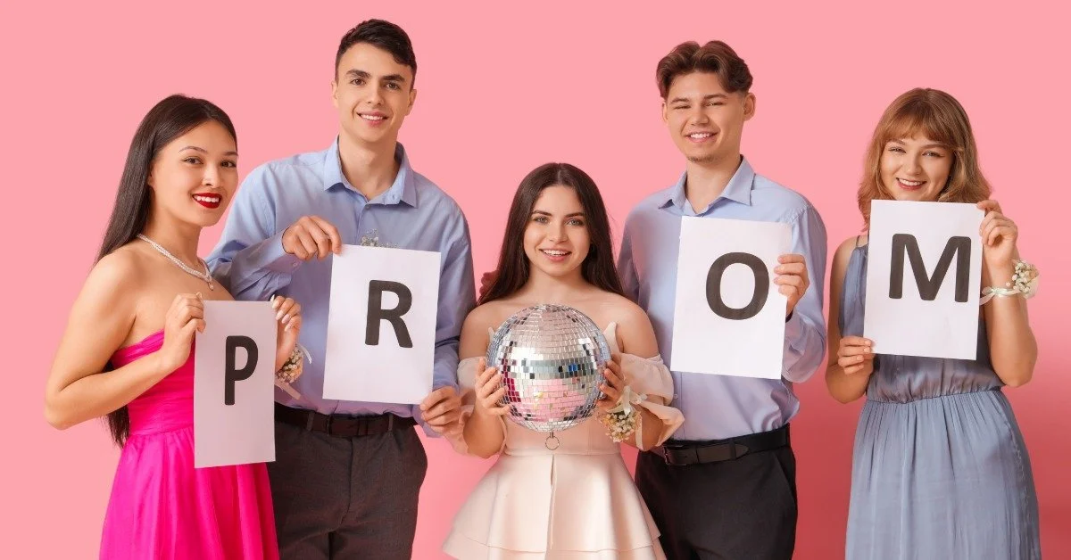Four teens in formal clothes hold signs that together spell the word “PROM." One additional teen holds a disco ball.
